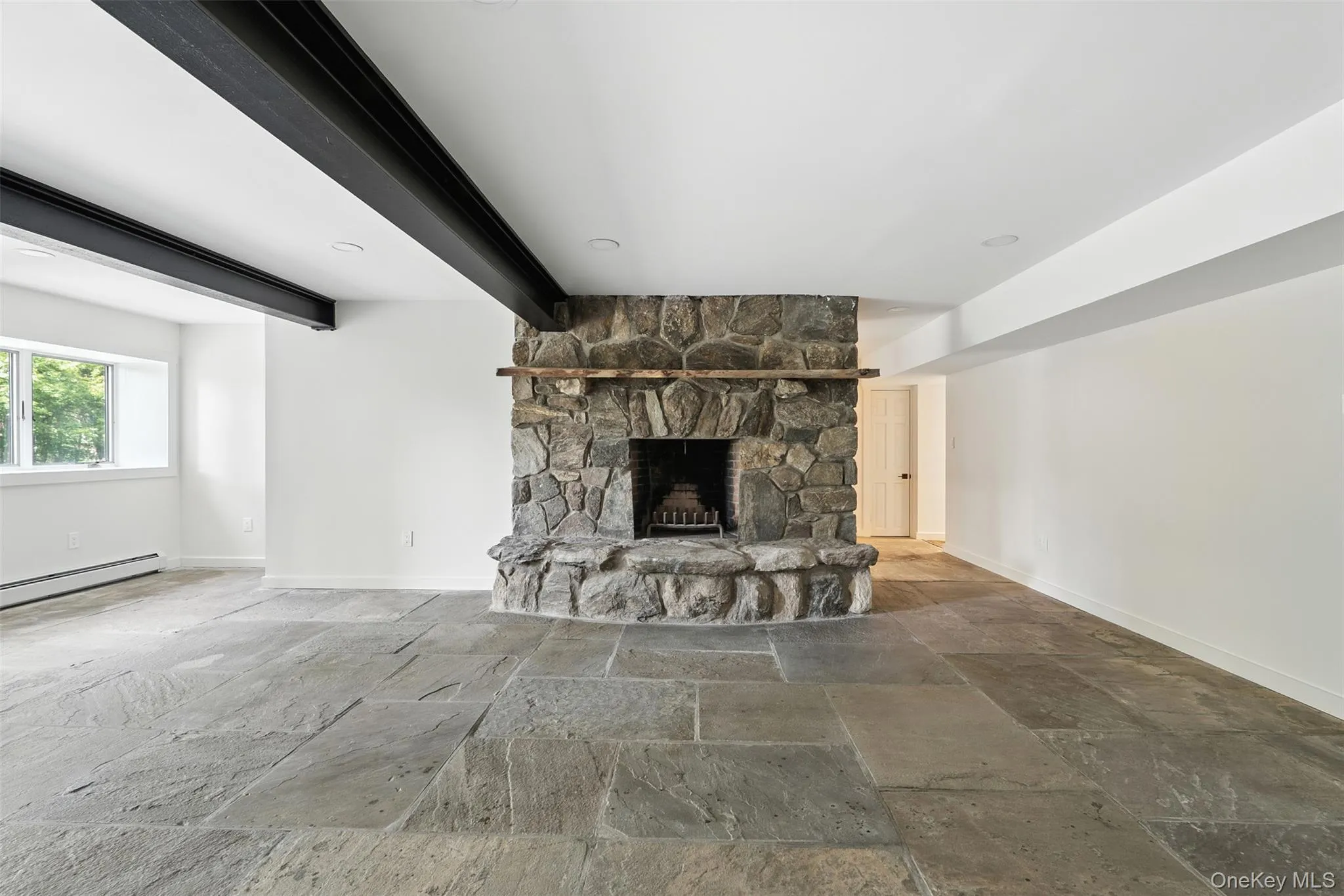 Unfurnished living room with stone tile flooring, a stone fireplace, and beam ceiling Unfurnished living room with stone tile flooring, a stone fireplace, and beam ceiling