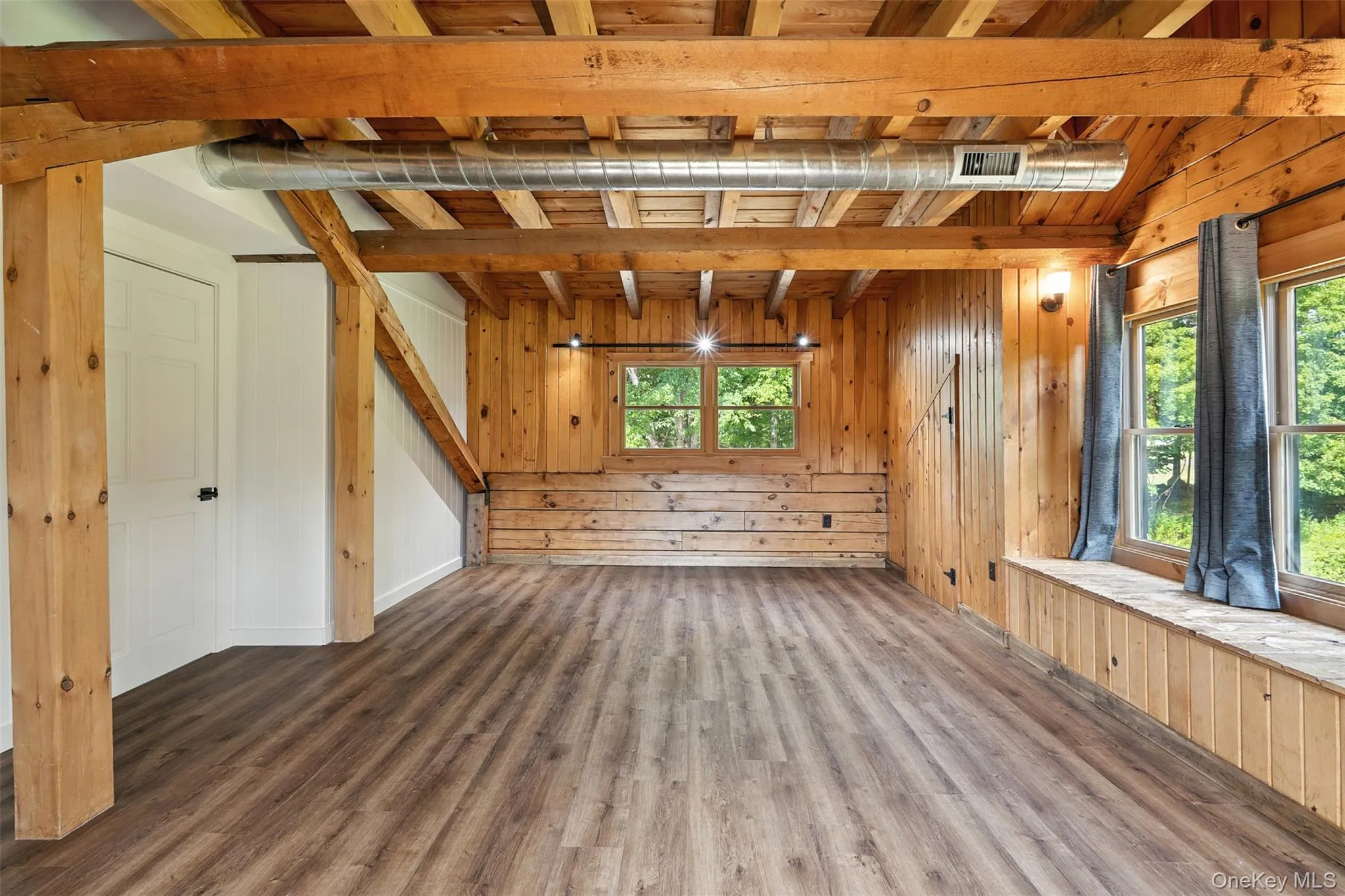 Unfurnished living room featuring wooden walls, wood finished floors, and beamed ceiling Unfurnished living room featuring wooden walls, wood finished floors, and beamed ceiling