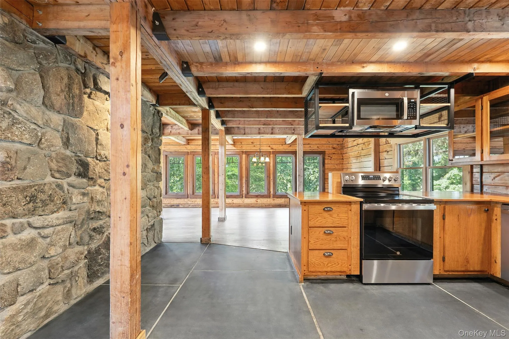 Kitchen with stainless steel appliances, finished concrete floors, brown cabinets, a wooden ceiling with exposed beams, and glass insert cabinets Kitchen with stainless steel appliances, finished concrete floors, brown cabinets, a wooden ceiling with exposed beams, and glass insert cabinets