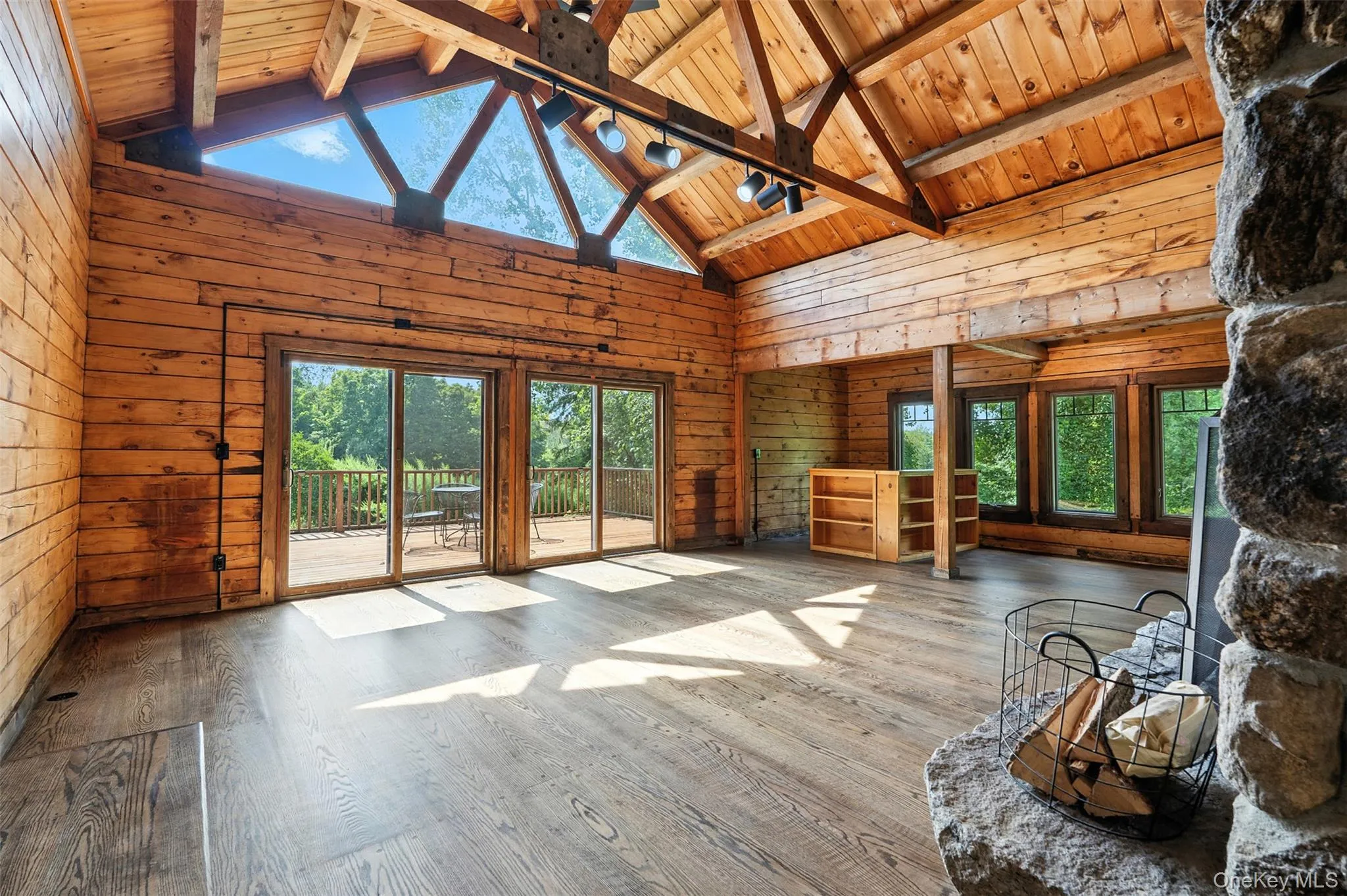 Unfurnished living room featuring high vaulted ceiling, wooden walls, wood finished floors, plenty of natural light, and a wooden ceiling with exposed beams Unfurnished living room featuring high vaulted ceiling, wooden walls, wood finished floors, plenty of natural light, and a wooden ceiling with exposed beams