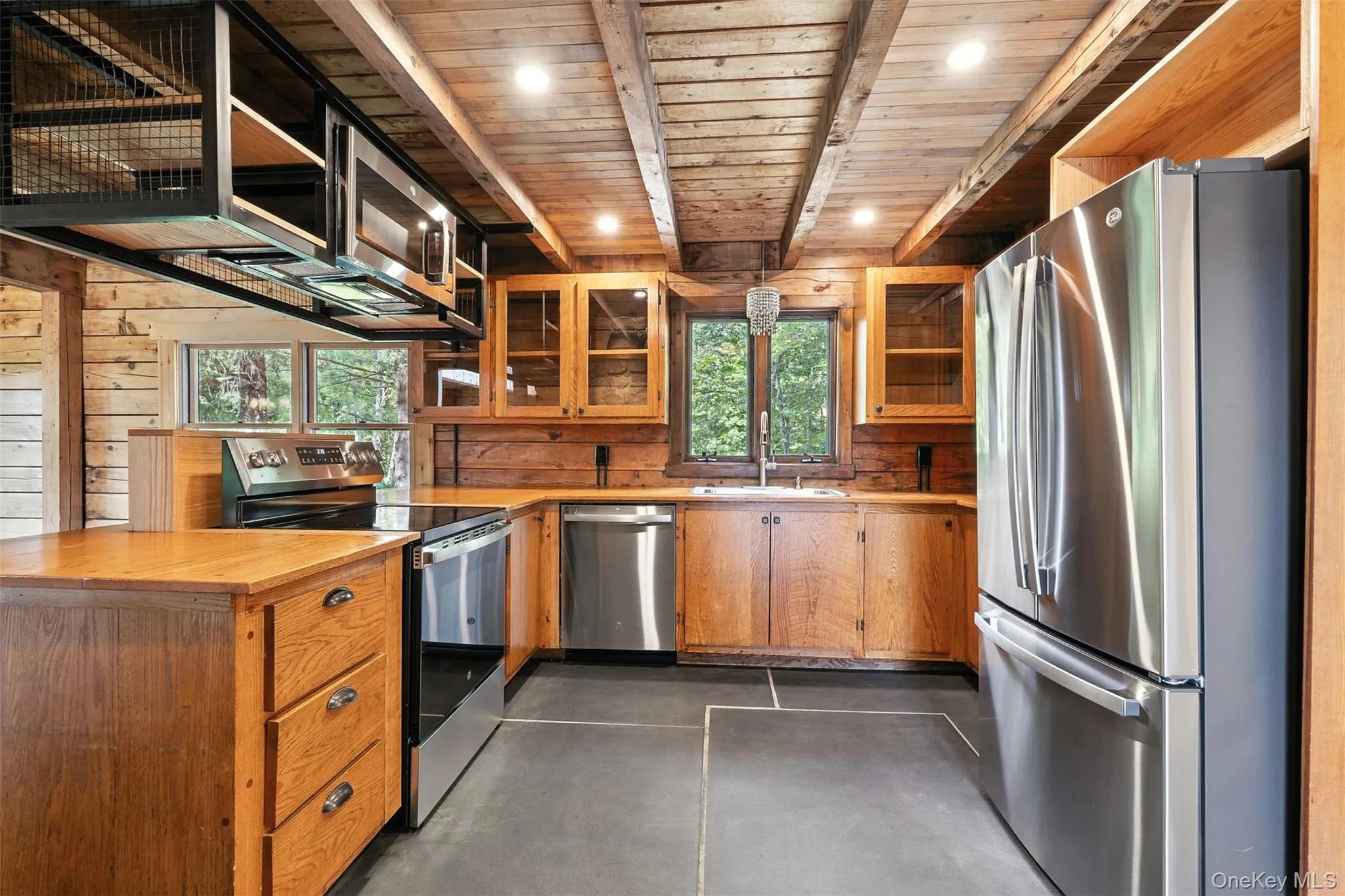Kitchen featuring stainless steel appliances, glass insert cabinets, a peninsula, butcher block counters, and a wooden ceiling with exposed beams Kitchen featuring stainless steel appliances, glass insert cabinets, a peninsula, butcher block counters, and a wooden ceiling with exposed beams