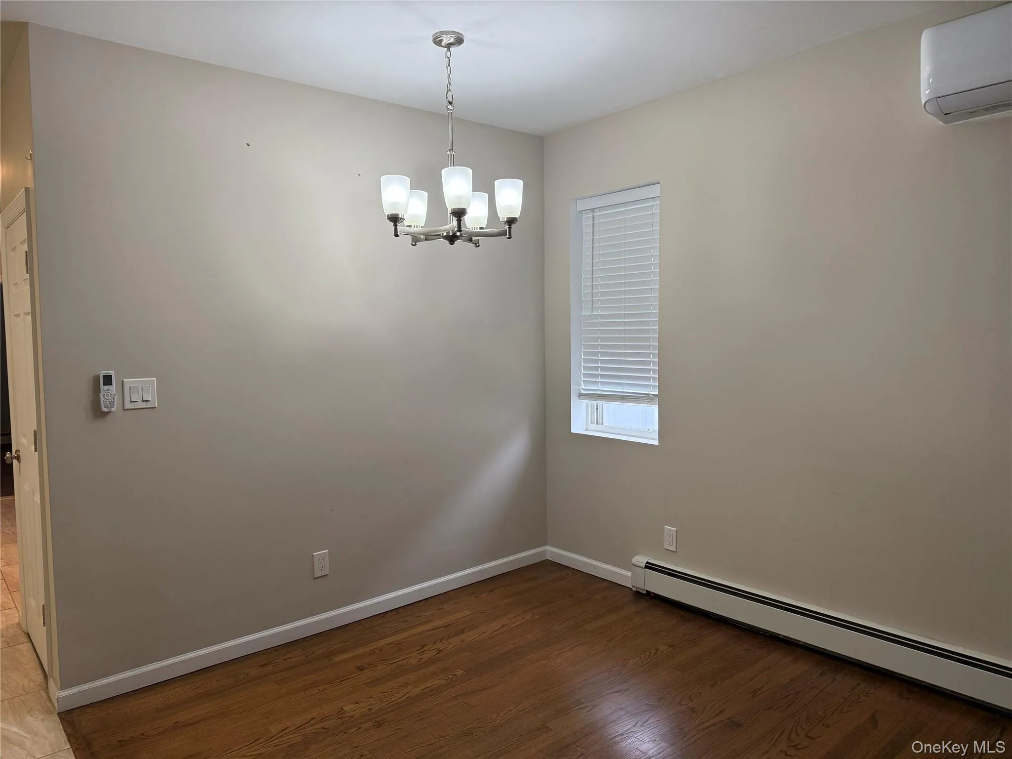 Spare room with a baseboard radiator, a wall mounted AC, dark wood-style floors, and a chandelier Spare room with a baseboard radiator, a wall mounted AC, dark wood-style floors, and a chandelier