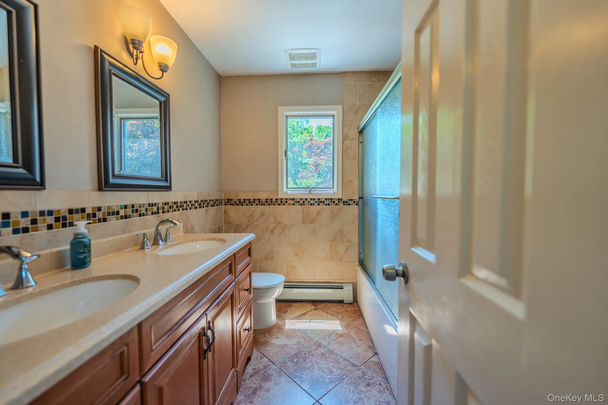 Bathroom featuring a dual vanity with light-colored countertops, wood-finish cabinetry, and two framed mirrors Bathroom featuring a dual vanity with light-colored countertops, wood-finish cabinetry, and two framed mirrors