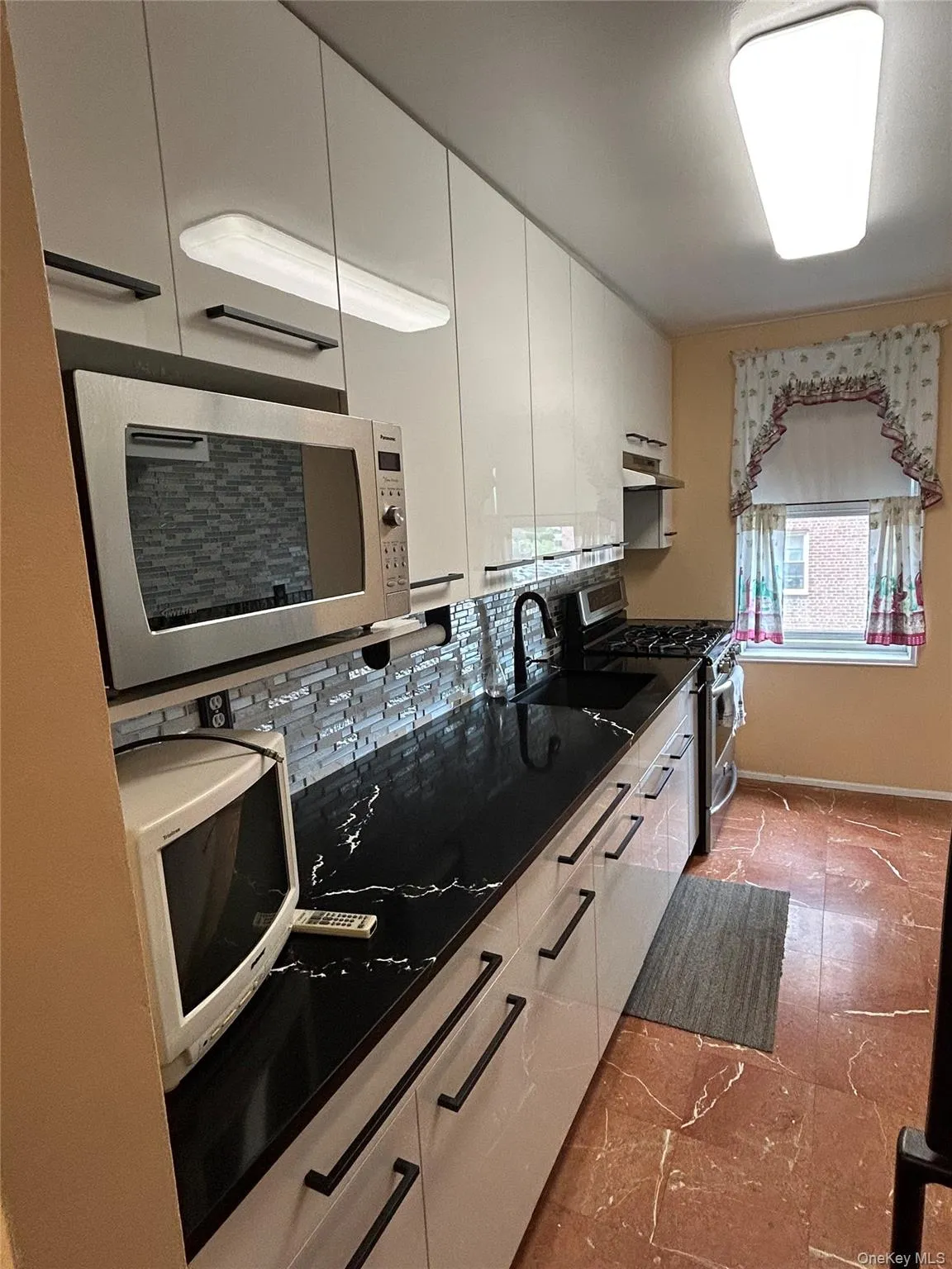 White cabinetry with black hardware, dark countertops, tiled backsplash, stainless steel range, and undermount farmhouse sink White cabinetry with black hardware, dark countertops, tiled backsplash, stainless steel range, and undermount farmhouse sink