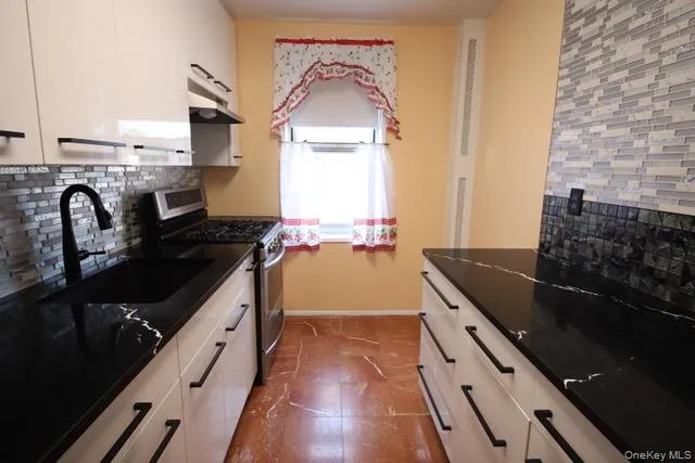 Kitchen featuring 3 stainless steel appliances, marble floors, extensive black countertops with white veining, white cabinetry with black hardware, and a mosaic tile backsplash Kitchen featuring 3 stainless steel appliances, marble floors, extensive black countertops with white veining, white cabinetry with black hardware, and a mosaic tile backsplash