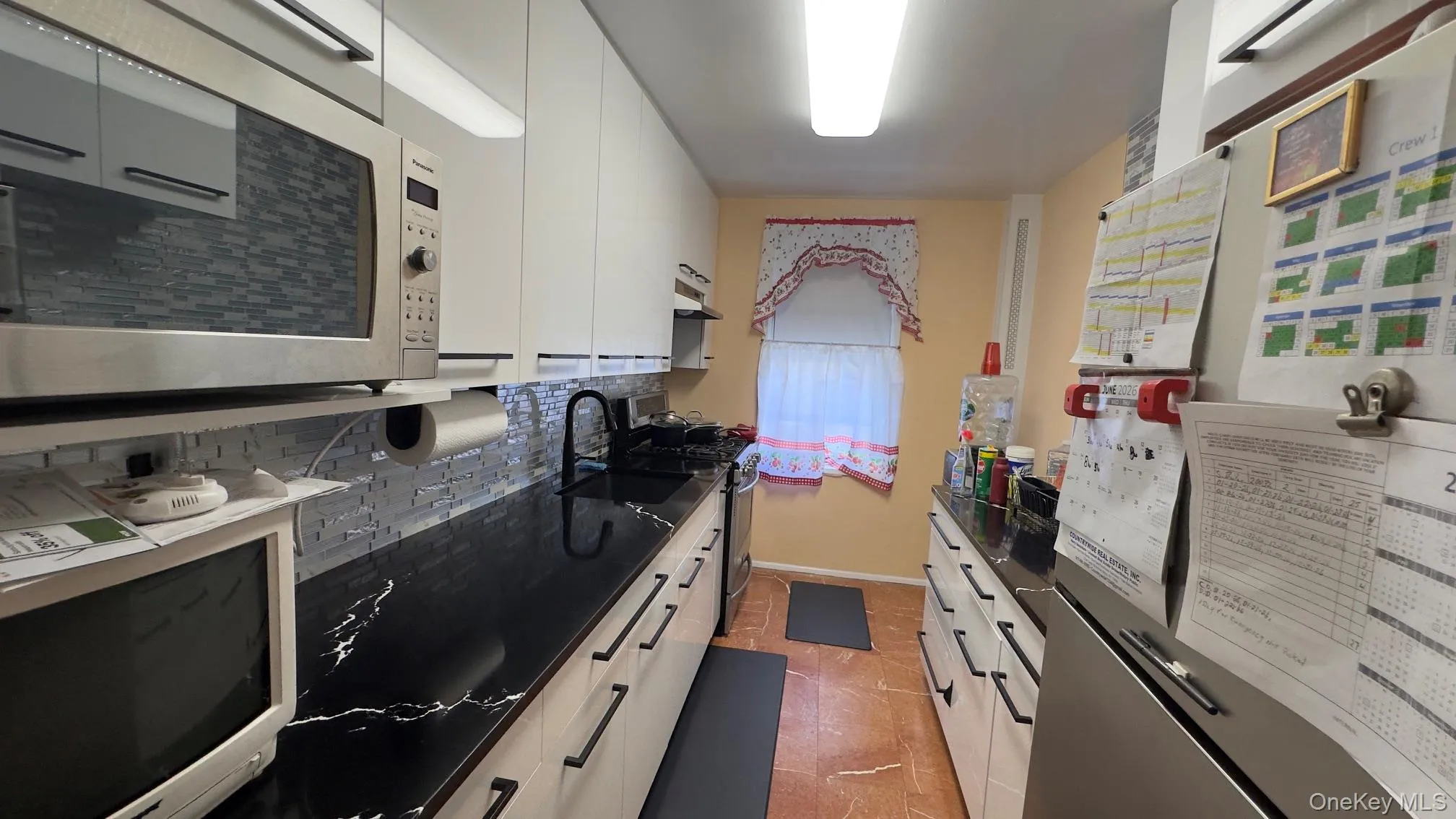 Kitchen featuring 3 stainless steel appliances, marble floors, extensive black countertops with white veining, white cabinetry with black hardware, and a mosaic tile backsplash Kitchen featuring 3 stainless steel appliances, marble floors, extensive black countertops with white veining, white cabinetry with black hardware, and a mosaic tile backsplash