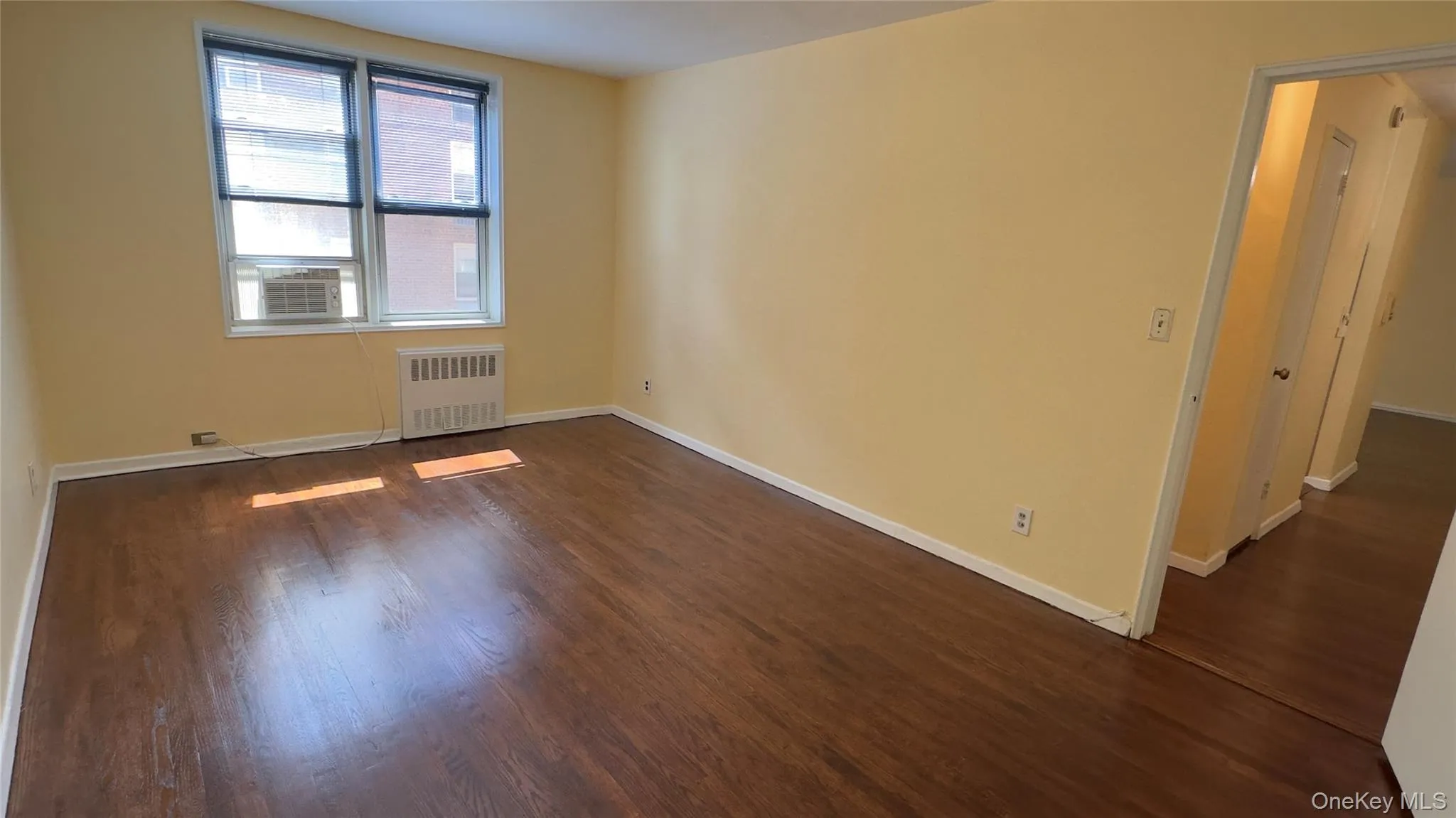 Rich wood-finish flooring, light-toned walls, and a large window with blue blinds Rich wood-finish flooring, light-toned walls, and a large window with blue blinds