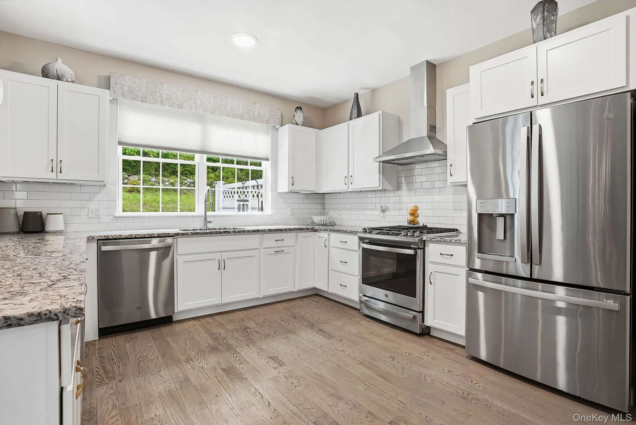 Modern kitchen featuring white shaker cabinetry, stainless steel appliances, speckled stone countertops, a subway tile backsplash, and light wood-finish flooring Modern kitchen featuring white shaker cabinetry, stainless steel appliances, speckled stone countertops, a subway tile backsplash, and light wood-finish flooring