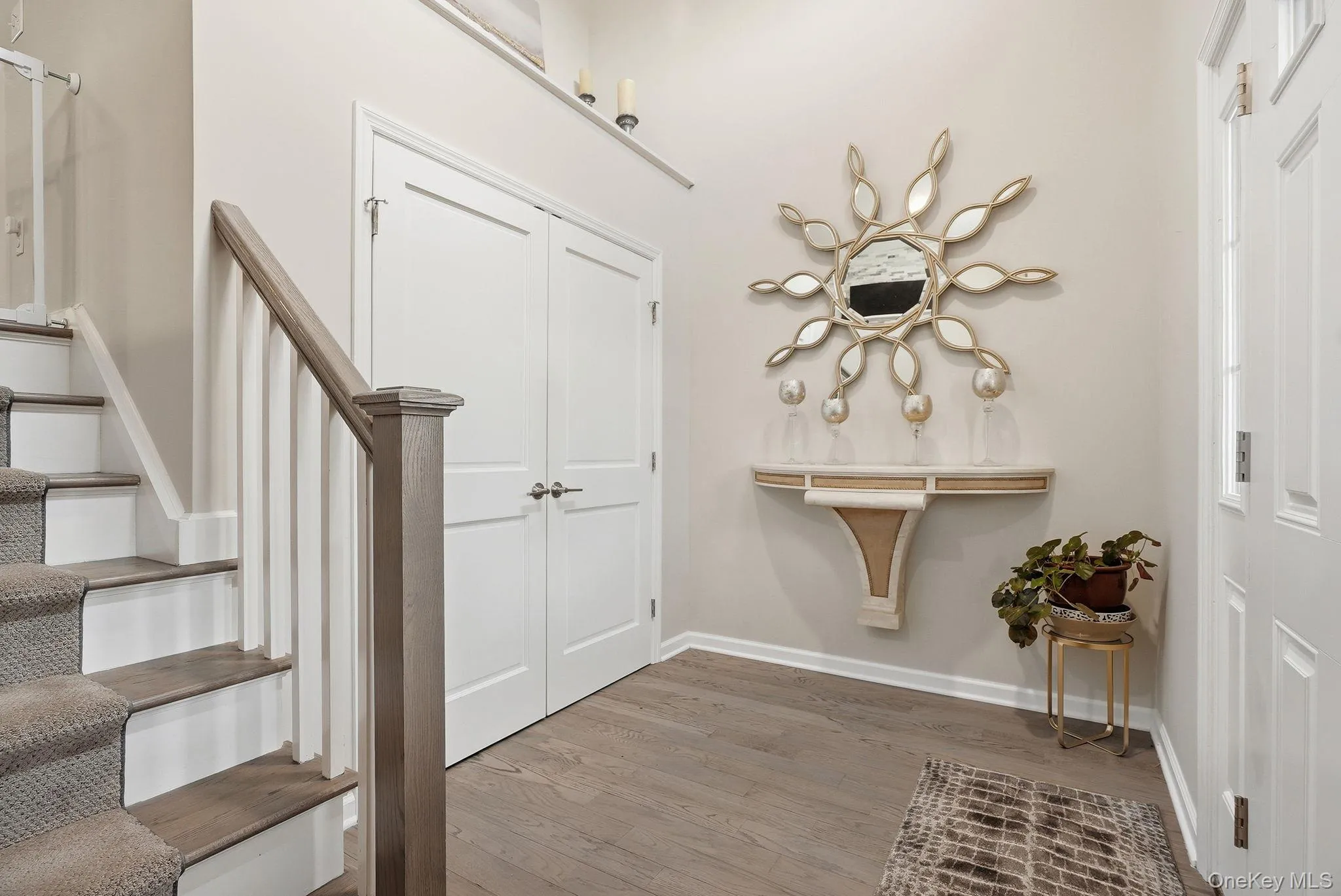 Entryway featuring wood-finish flooring, a staircase with carpeted treads and wood handrail, double panel doors, and a decorative wall shelf Entryway featuring wood-finish flooring, a staircase with carpeted treads and wood handrail, double panel doors, and a decorative wall shelf