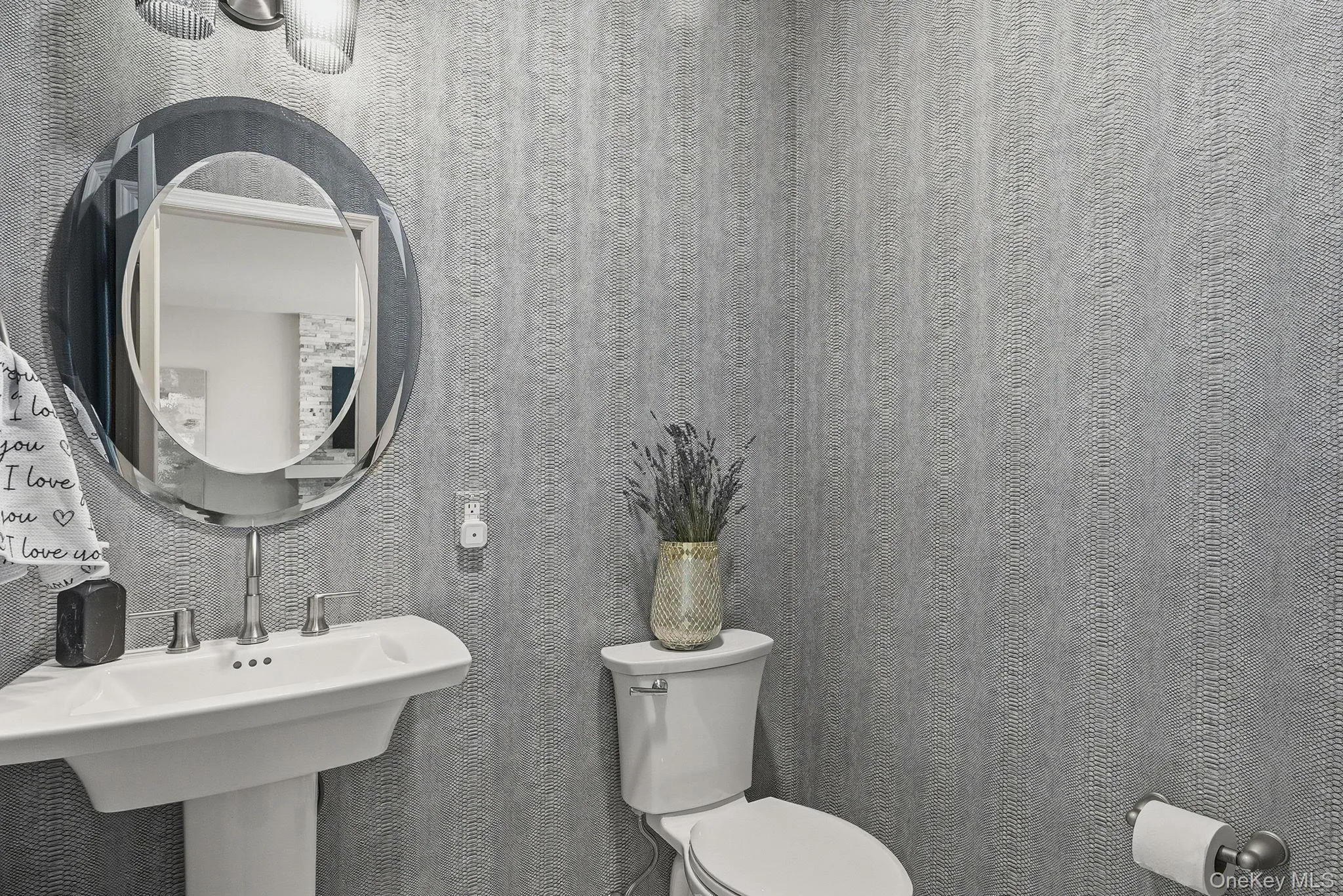 Downstairs half bath featuring pedestal sink with a polished chrome faucet and an oval decorative mirror Downstairs half bath featuring pedestal sink with a polished chrome faucet and an oval decorative mirror