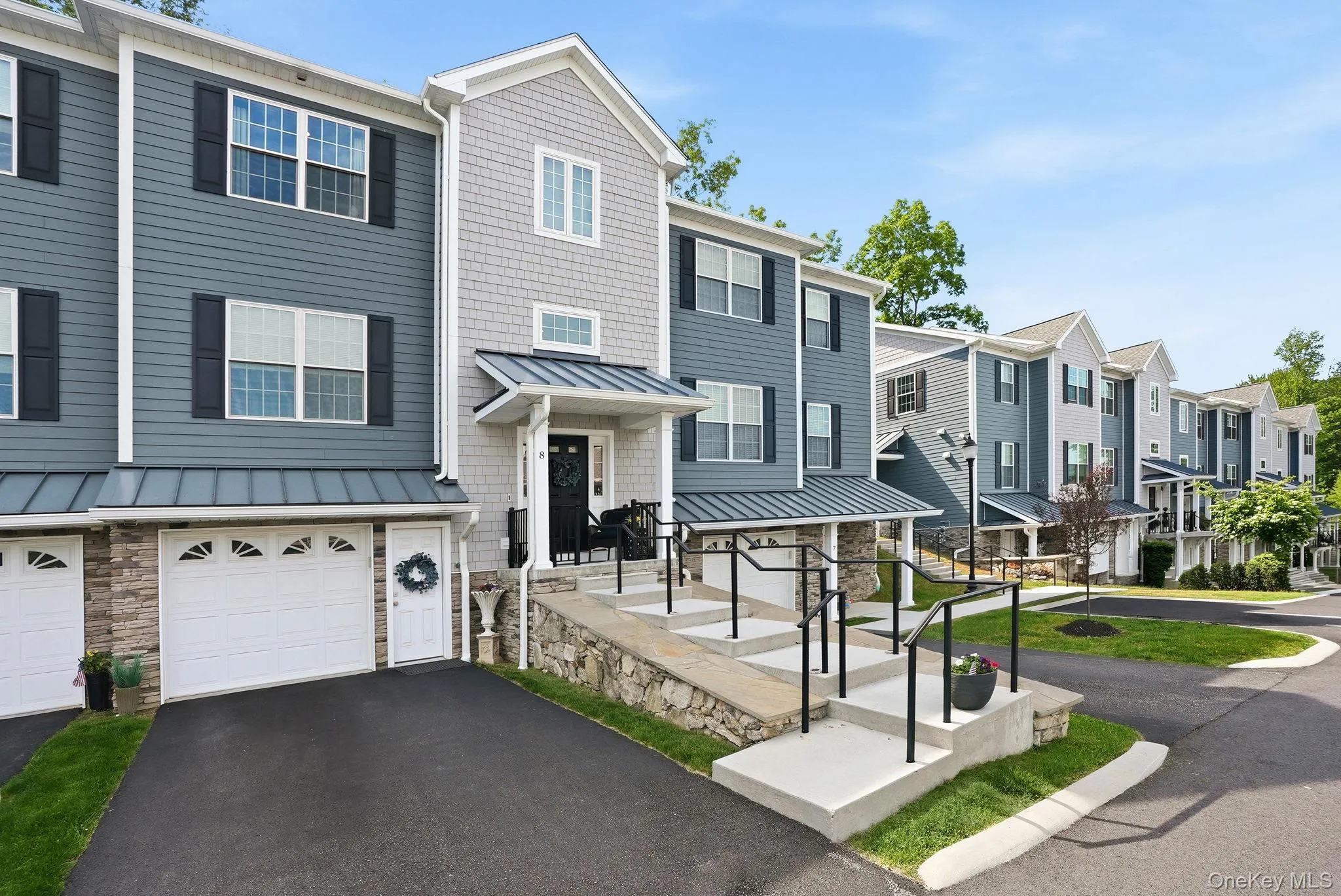 Multi-level townhome featuring a stone and siding exterior, a private garage, and a covered front entry porch with black railings Multi-level townhome featuring a stone and siding exterior, a private garage, and a covered front entry porch with black railings