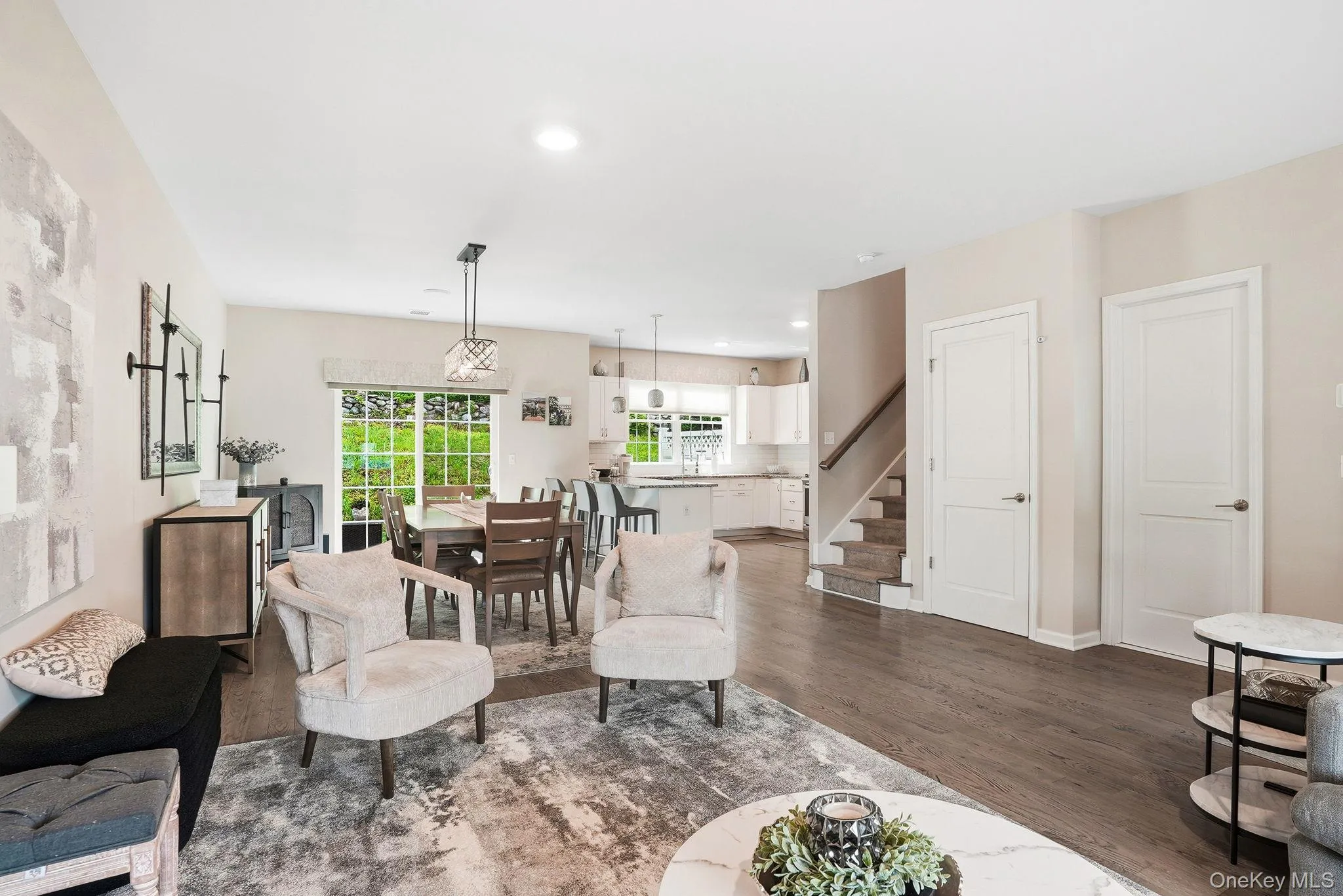 Open-concept main living area featuring wood-finish flooring, recessed lighting, and a dining space with an ornate chandelier and large window Open-concept main living area featuring wood-finish flooring, recessed lighting, and a dining space with an ornate chandelier and large window