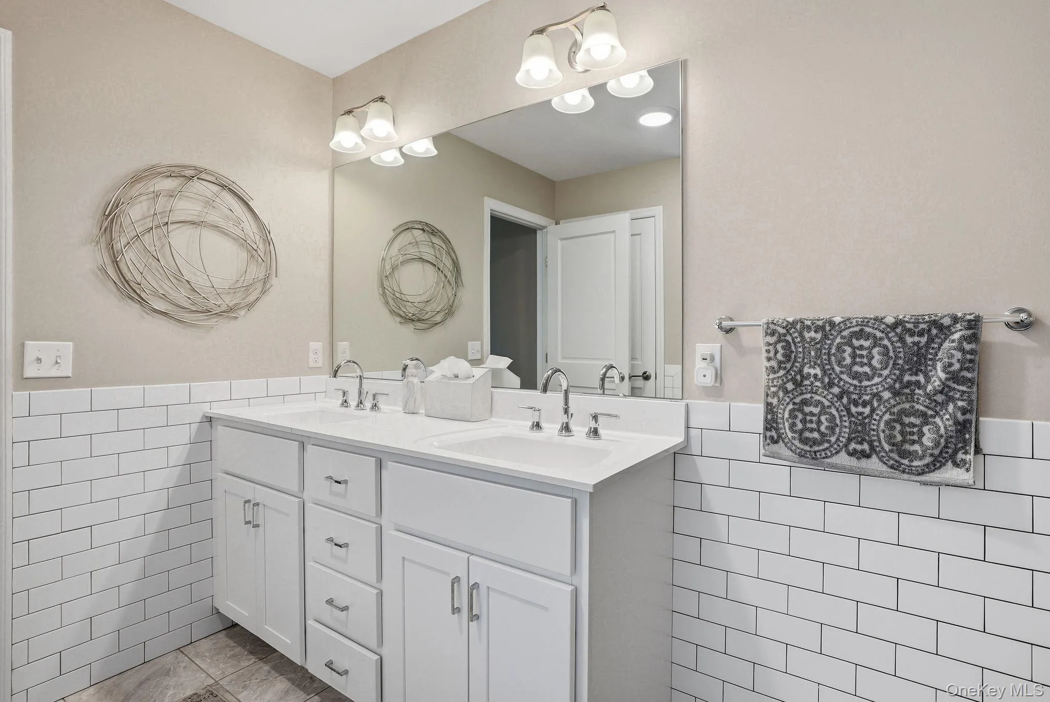 Primary bathroom featuring double vanity with white cabinetry and chrome hardware, featuring two undermount sinks and a large framed mirror Primary bathroom featuring double vanity with white cabinetry and chrome hardware, featuring two undermount sinks and a large framed mirror