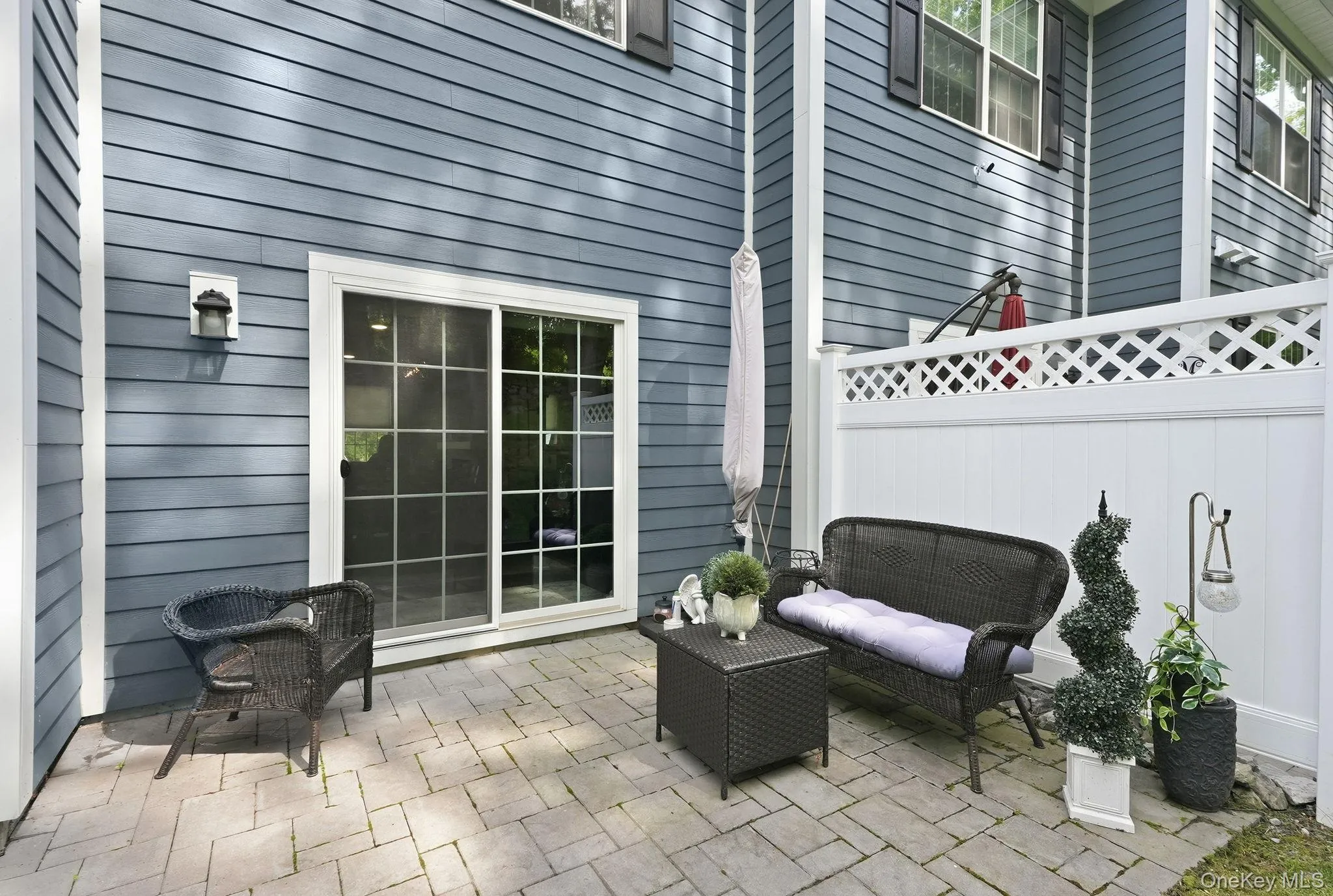 Private paver patio featuring a sliding glass door entry, white lattice fencing, and exterior wall lantern Private paver patio featuring a sliding glass door entry, white lattice fencing, and exterior wall lantern