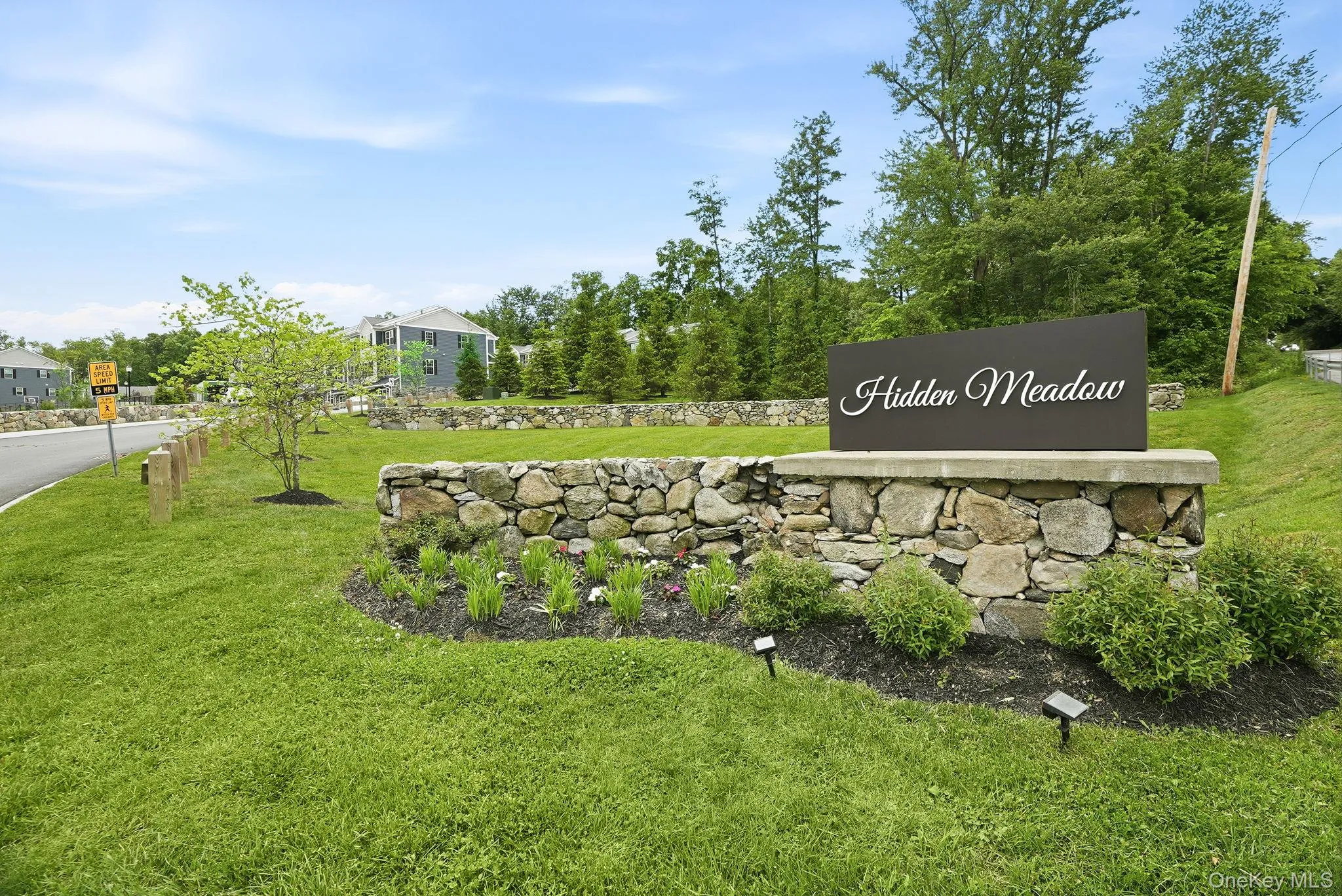 Entry sign featuring a stone wall foundation, dark sign panel with script lettering, and surrounding landscaping Entry sign featuring a stone wall foundation, dark sign panel with script lettering, and surrounding landscaping