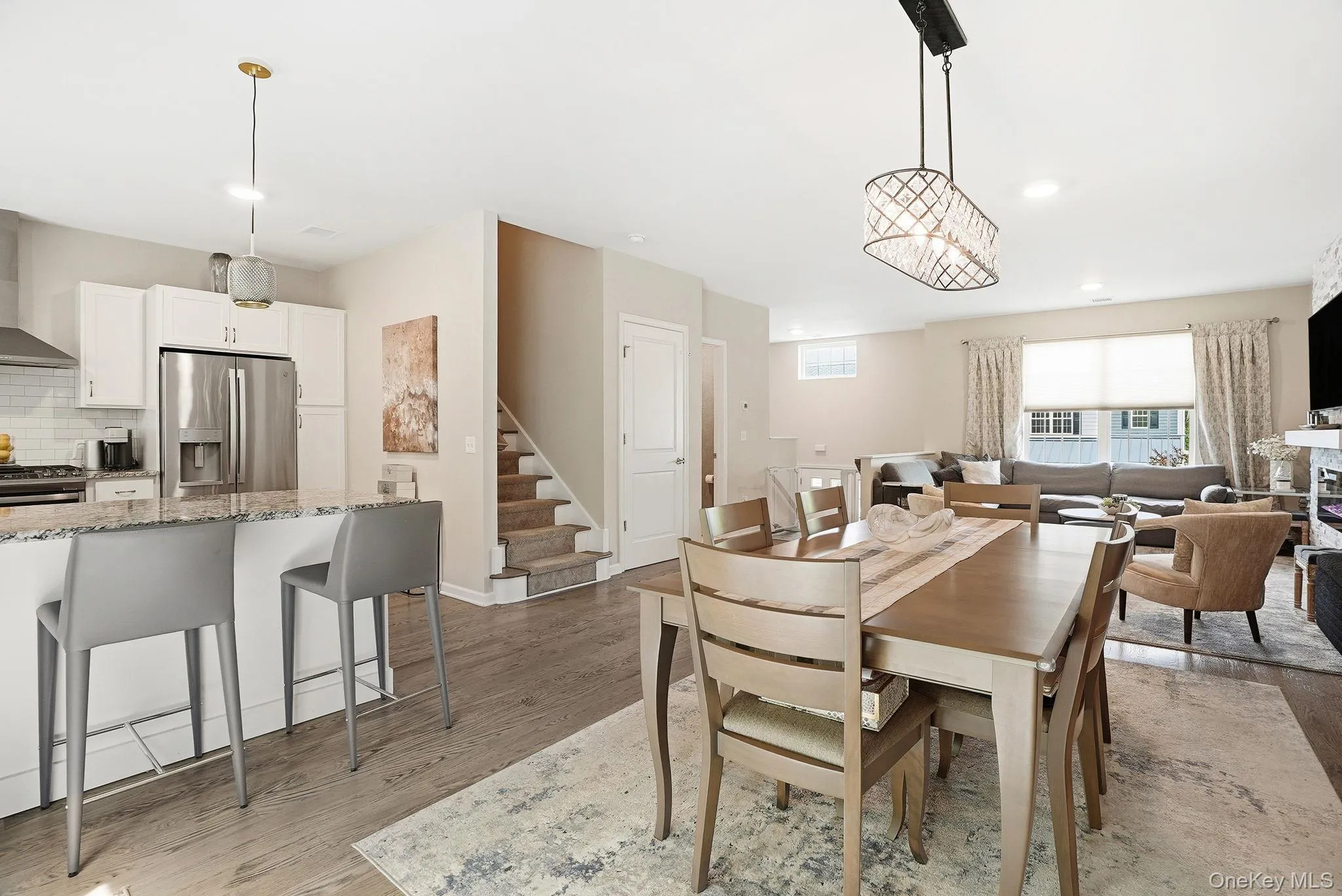 Open-concept living space featuring wood-finish flooring, recessed lighting, a modern kitchen island with seating, stainless steel appliances, and a tiled backsplash Open-concept living space featuring wood-finish flooring, recessed lighting, a modern kitchen island with seating, stainless steel appliances, and a tiled backsplash