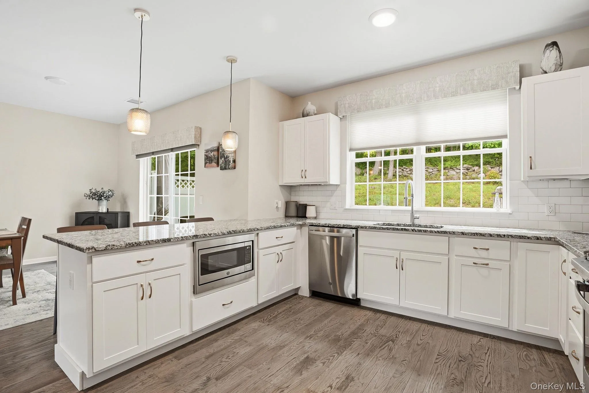 Modern kitchen featuring white shaker cabinetry, stainless steel appliances, speckled stone countertops, and wood-finish flooring Modern kitchen featuring white shaker cabinetry, stainless steel appliances, speckled stone countertops, and wood-finish flooring