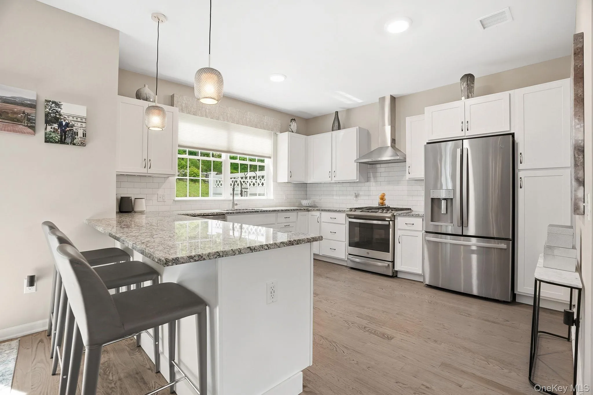 Modern kitchen featuring white cabinetry, light-toned wood-finish flooring, stainless steel appliances, a white subway tile backsplash, and a large central island with a light-colored countertop Modern kitchen featuring white cabinetry, light-toned wood-finish flooring, stainless steel appliances, a white subway tile backsplash, and a large central island with a light-colored countertop
