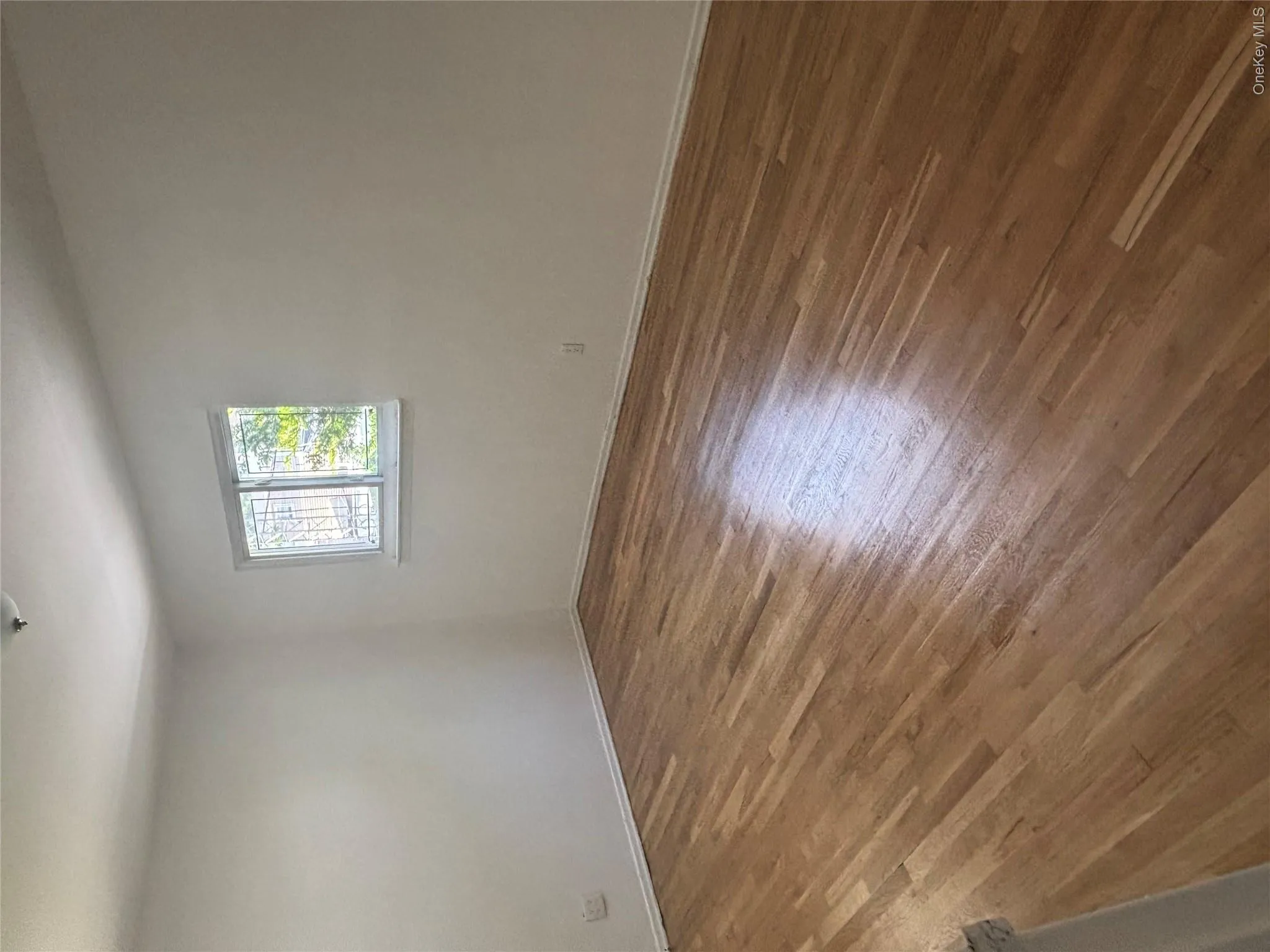 Light wood-finish flooring, white painted walls, and a window with security bars Light wood-finish flooring, white painted walls, and a window with security bars