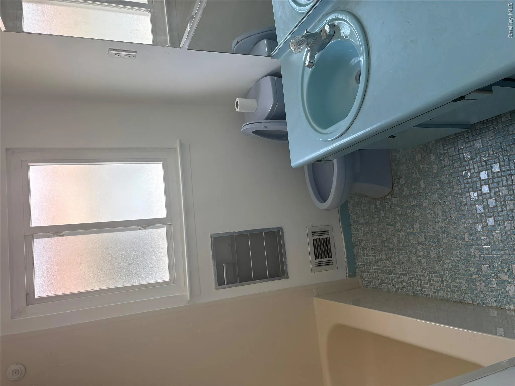 Bathroom featuring a single window with frosted panes, a built-in bathtub, a vanity with an integrated basin, a mirrored medicine cabinet, and patterned mosaic tile flooring Bathroom featuring a single window with frosted panes, a built-in bathtub, a vanity with an integrated basin, a mirrored medicine cabinet, and patterned mosaic tile flooring