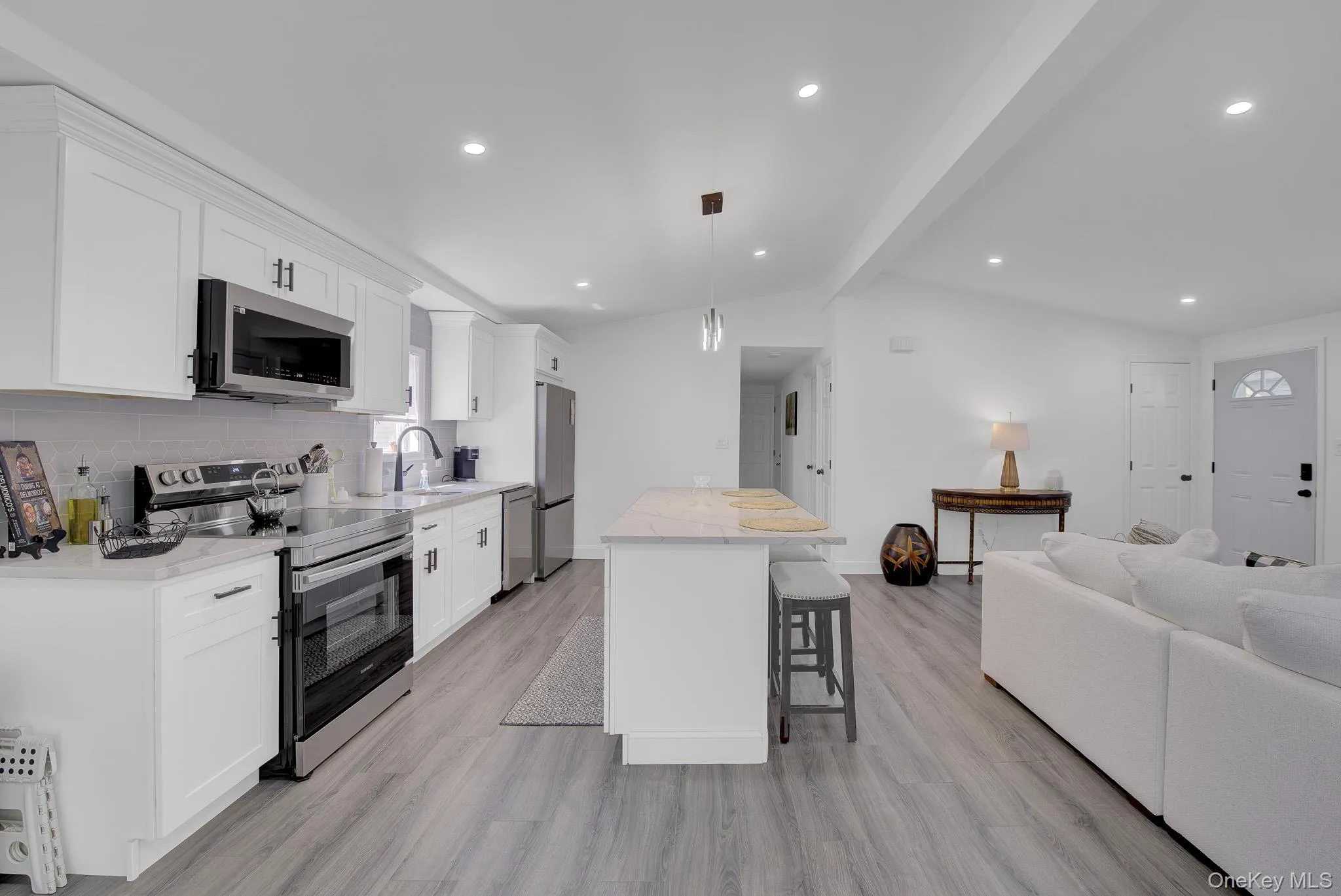Modern kitchen featuring white cabinetry, stainless steel appliances, light-toned countertops, a subway tile backsplash, and an island with seating Modern kitchen featuring white cabinetry, stainless steel appliances, light-toned countertops, a subway tile backsplash, and an island with seating