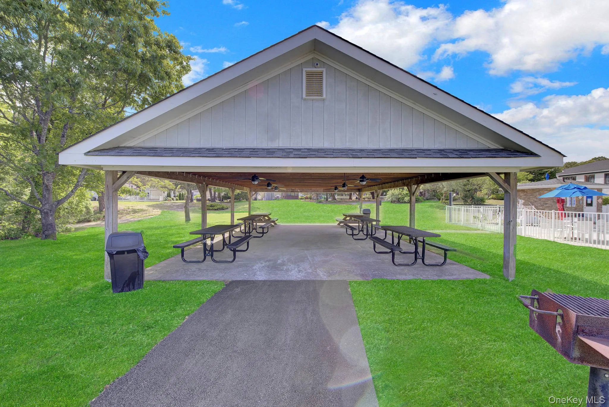 Expansive covered pavilion featuring multiple picnic tables, a concrete slab, and overhead lighting Expansive covered pavilion featuring multiple picnic tables, a concrete slab, and overhead lighting