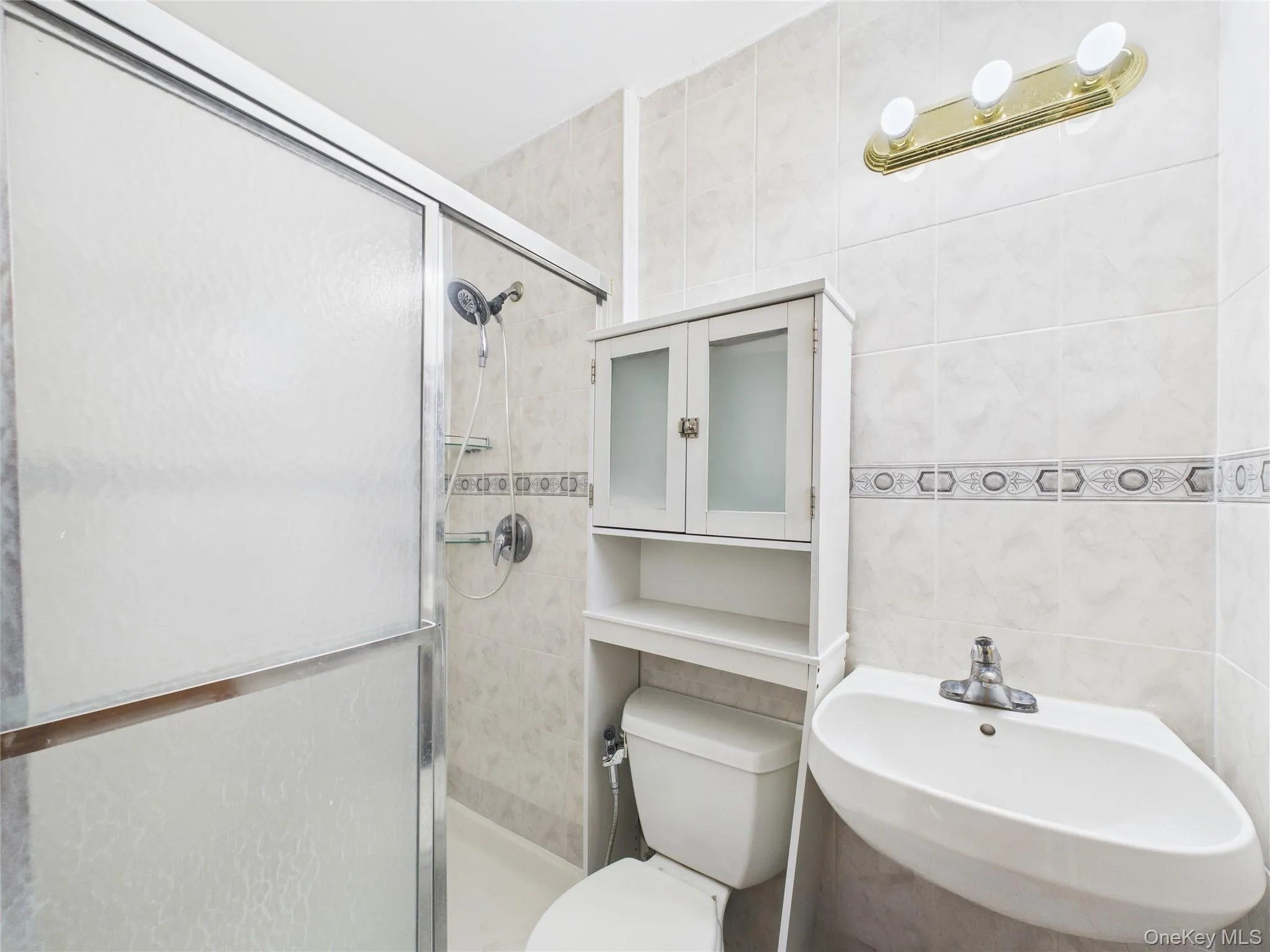 Full bathroom with a stall shower, a sink, toilet, and tile walls Full bathroom with a stall shower, a sink, toilet, and tile walls