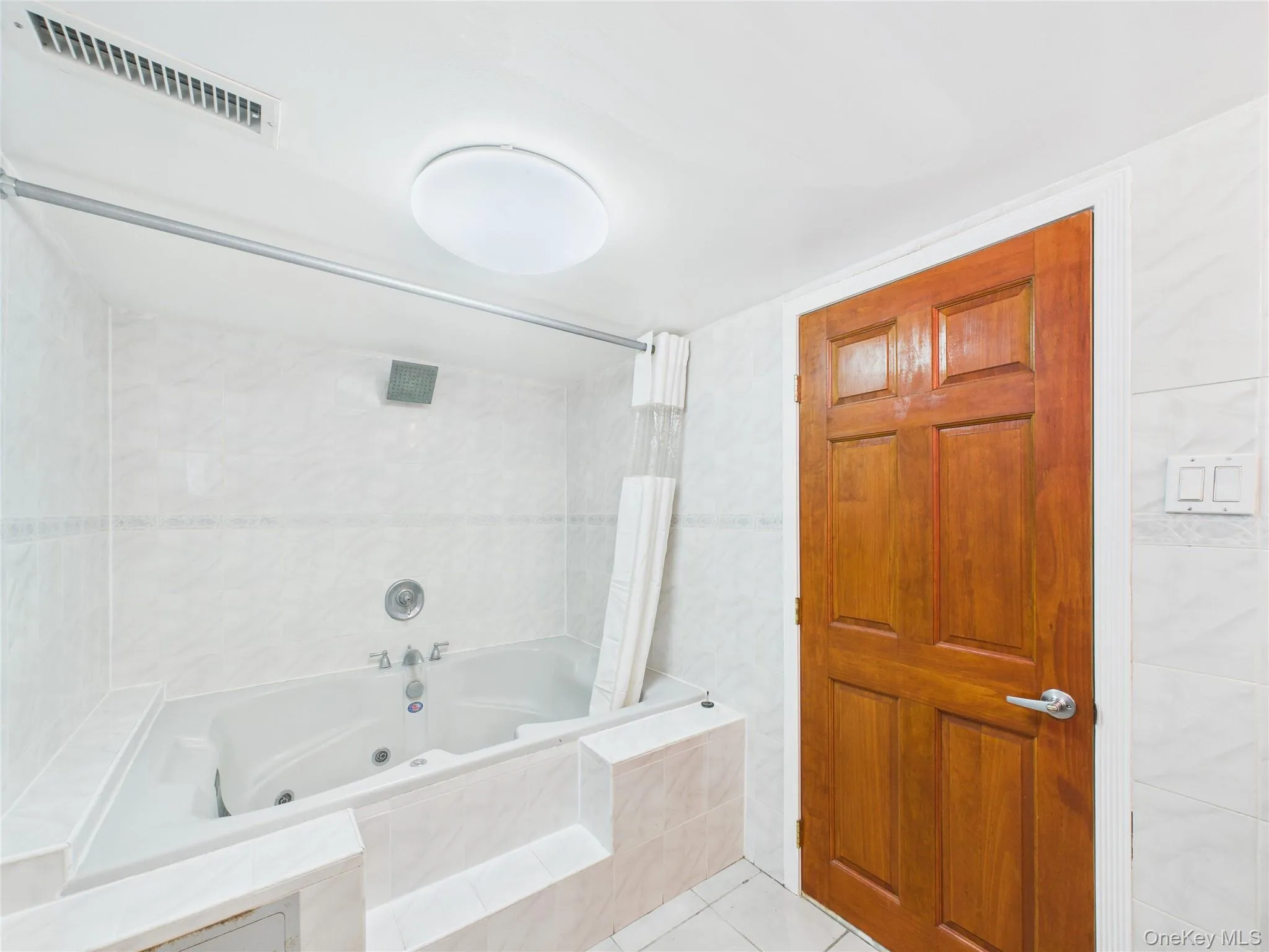 Bathroom with a combined bath / shower with jetted tub, tile patterned flooring, and tile walls Bathroom with a combined bath / shower with jetted tub, tile patterned flooring, and tile walls