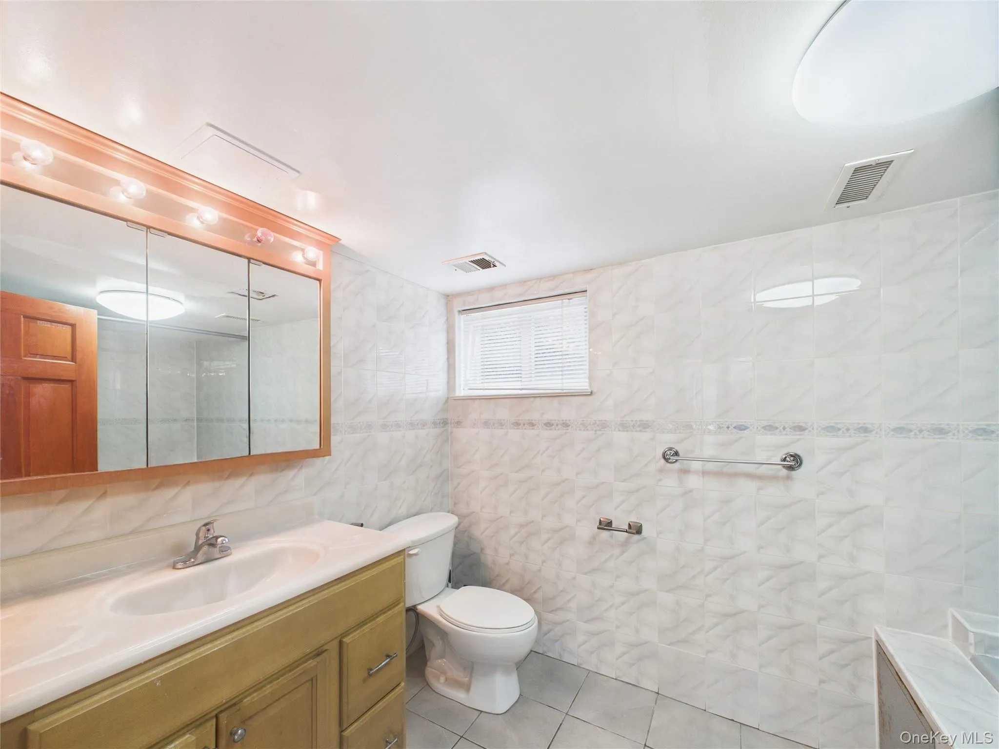 Bathroom featuring vanity, tile walls, tile patterned floors, and toilet Bathroom featuring vanity, tile walls, tile patterned floors, and toilet