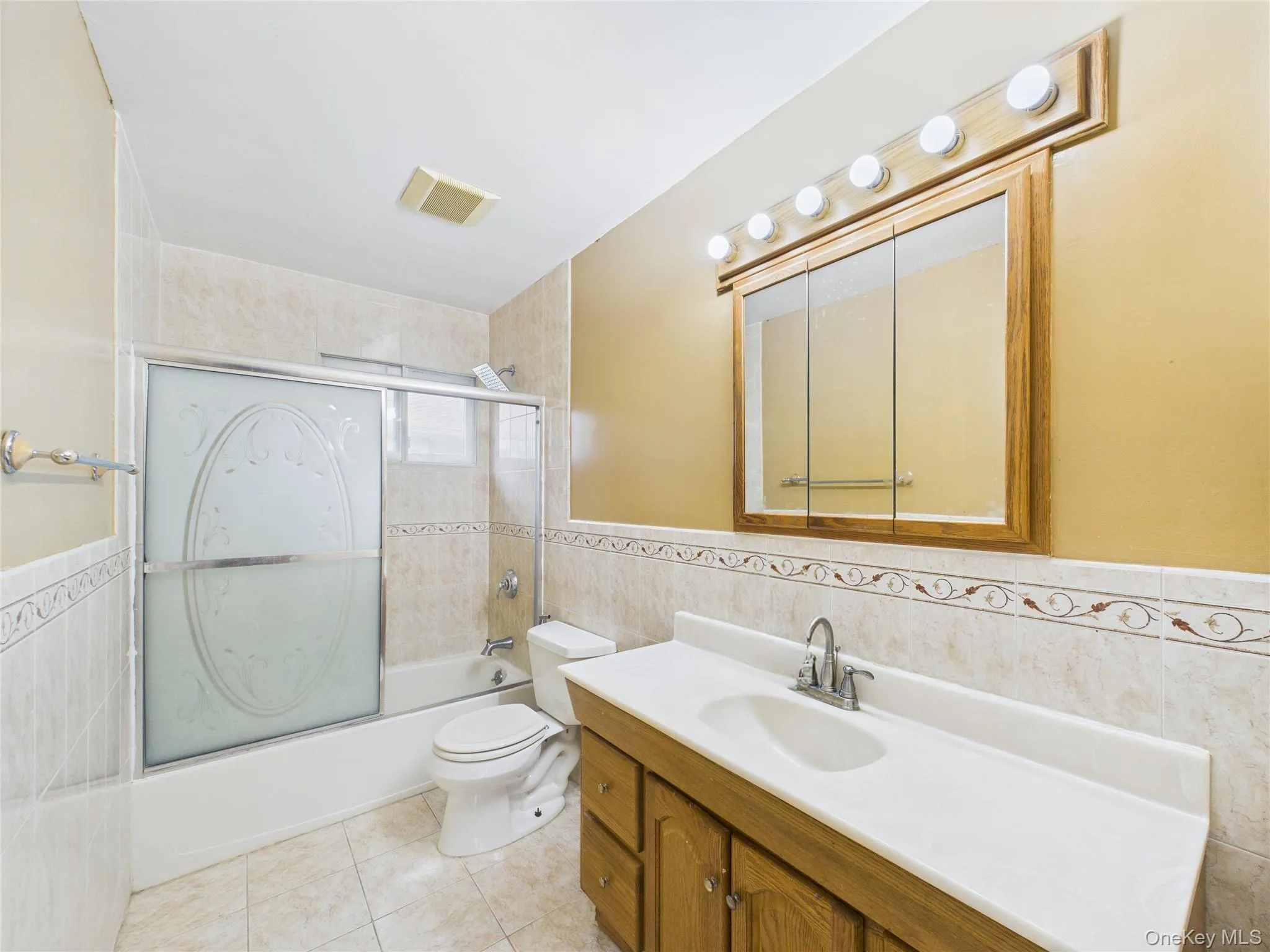 Full bath featuring tile walls, tile patterned floors, combined bath / shower with glass door, vanity, and toilet Full bath featuring tile walls, tile patterned floors, combined bath / shower with glass door, vanity, and toilet