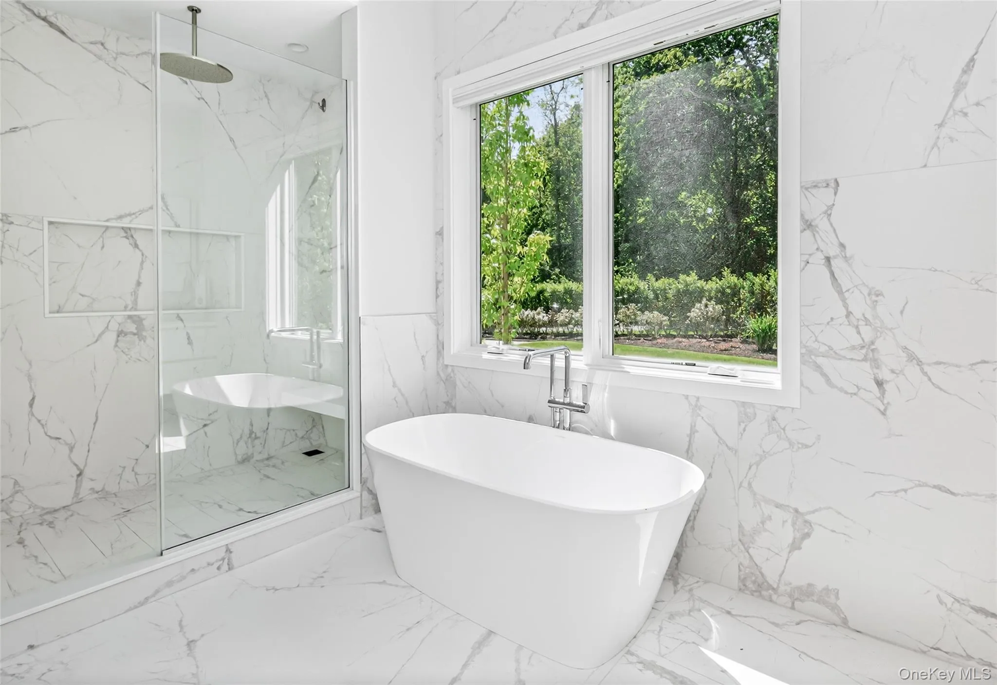 Bathroom featuring a freestanding soaking tub with floor-mounted faucet, a walk-in shower with a built-in bench and rainfall showerhead, and expansive window Bathroom featuring a freestanding soaking tub with floor-mounted faucet, a walk-in shower with a built-in bench and rainfall showerhead, and expansive window