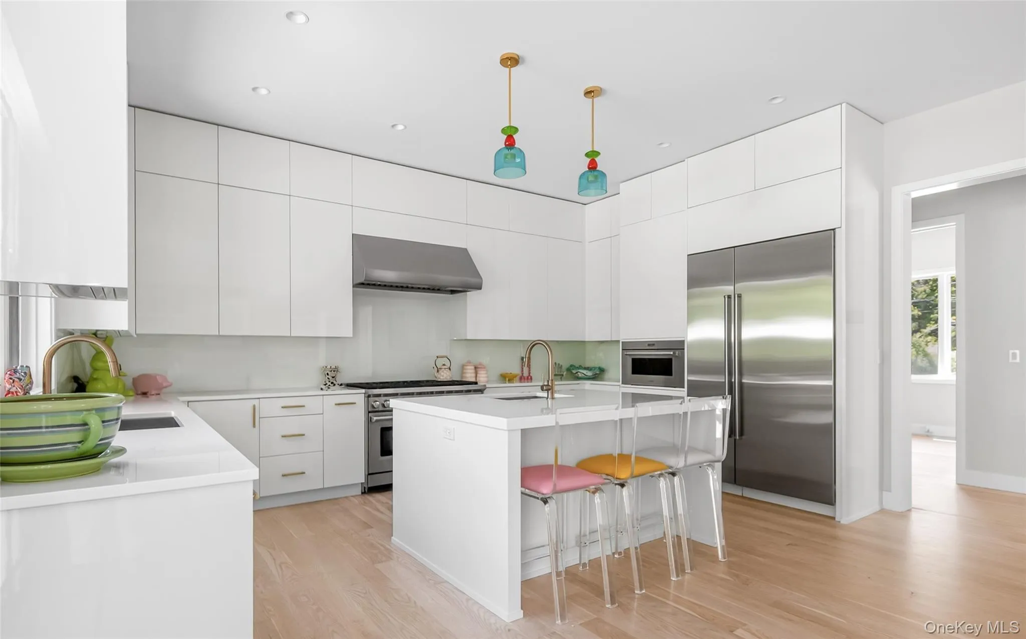 Bright kitchen featuring extensive white cabinetry, a central island with countertop seating, stainless steel appliances, light wood-finish flooring, and recessed ceiling lighting Bright kitchen featuring extensive white cabinetry, a central island with countertop seating, stainless steel appliances, light wood-finish flooring, and recessed ceiling lighting