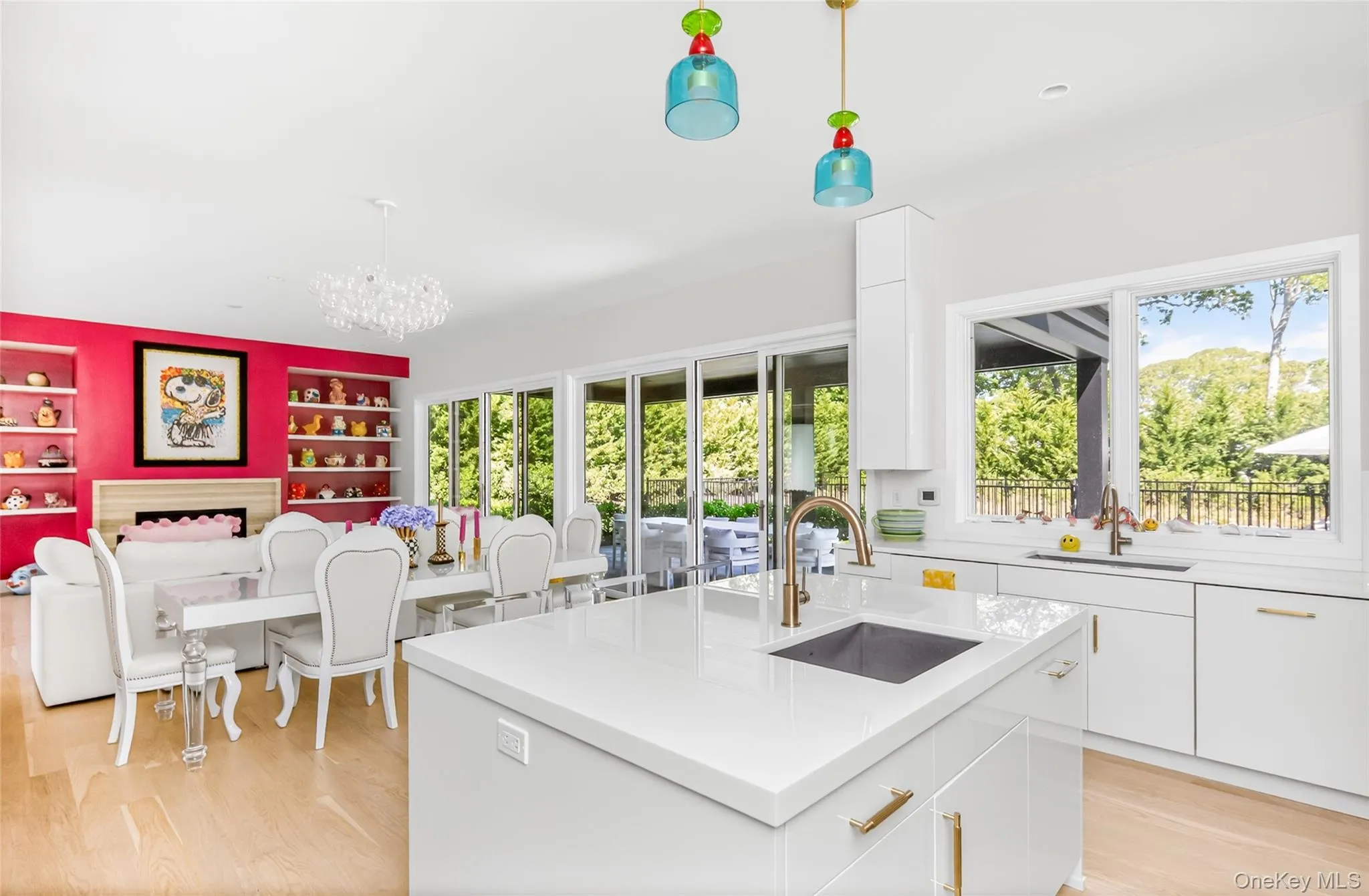 Open-concept kitchen featuring an island with an undermount sink, white cabinetry with brass hardware, and light wood-finish flooring Open-concept kitchen featuring an island with an undermount sink, white cabinetry with brass hardware, and light wood-finish flooring