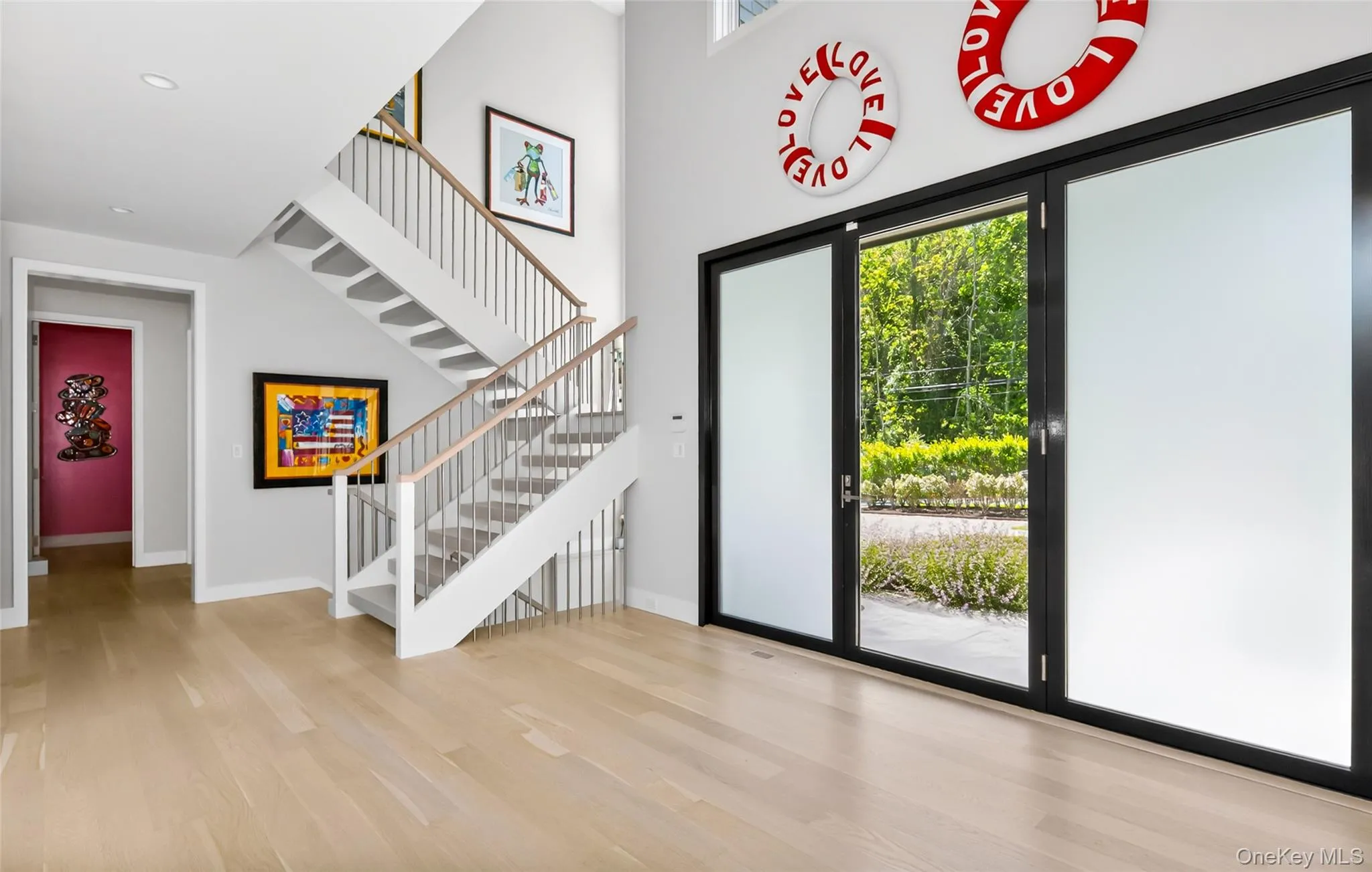 Grand entry featuring a light wood-finish flooring, a contemporary staircase with wood handrails and white risers, and tall ceilings Grand entry featuring a light wood-finish flooring, a contemporary staircase with wood handrails and white risers, and tall ceilings