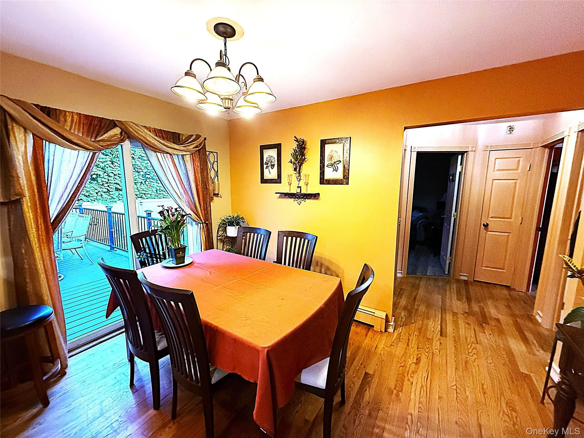 Interior dining area featuring wood-finish flooring, a multi-light chandelier, and sliding glass doors leading to an exterior deck Interior dining area featuring wood-finish flooring, a multi-light chandelier, and sliding glass doors leading to an exterior deck