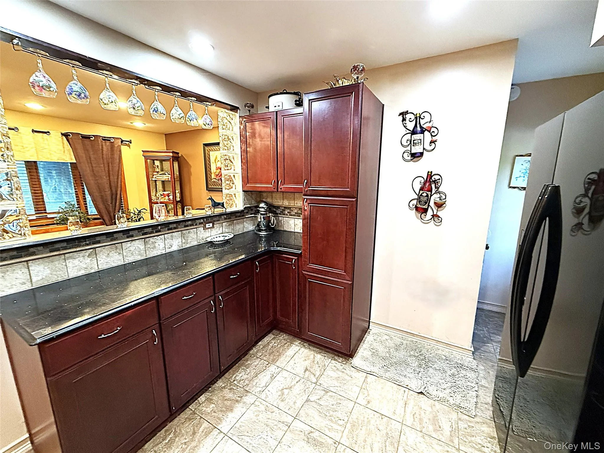 Kitchen featuring dark wood-finish cabinetry, dark countertops, a tiled backsplash, and light-toned floor tiles Kitchen featuring dark wood-finish cabinetry, dark countertops, a tiled backsplash, and light-toned floor tiles