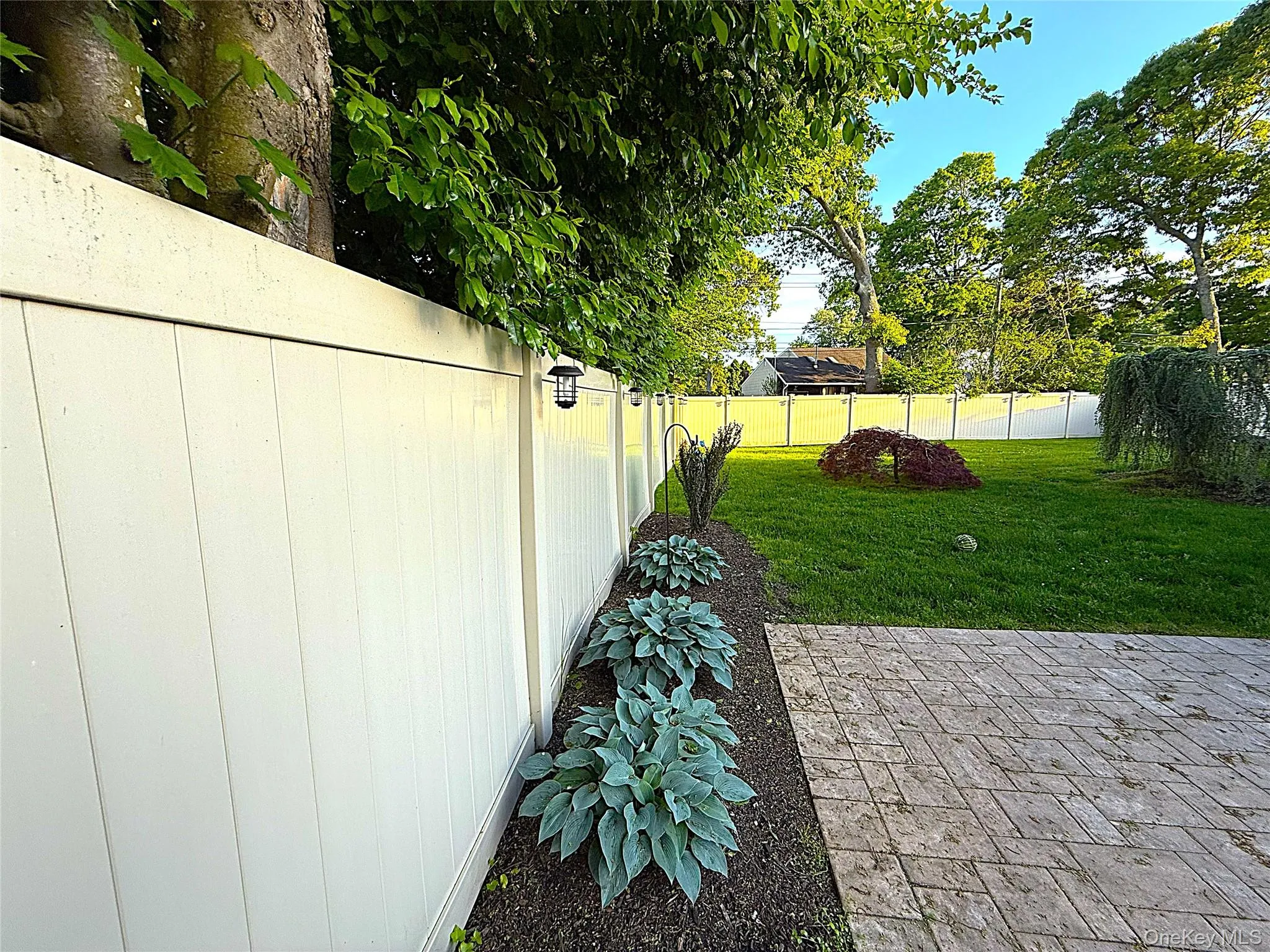 Patio featuring paver flooring, bordered by a garden bed with hostas Patio featuring paver flooring, bordered by a garden bed with hostas