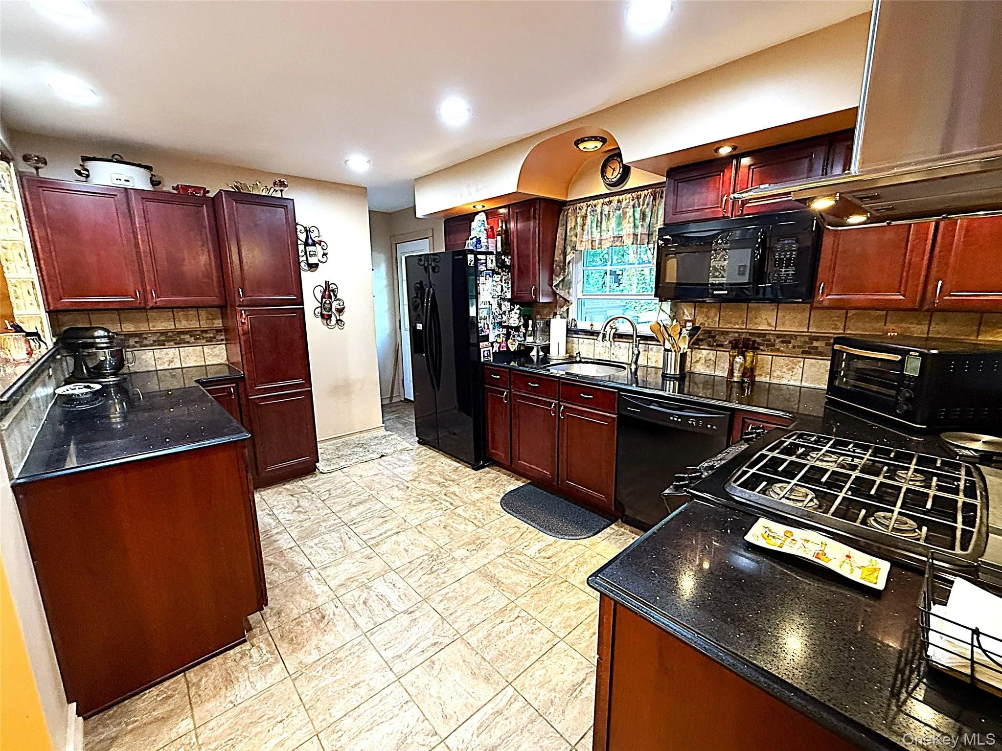 Kitchen featuring rich wood cabinetry, black countertops, and a tiled backsplash Kitchen featuring rich wood cabinetry, black countertops, and a tiled backsplash