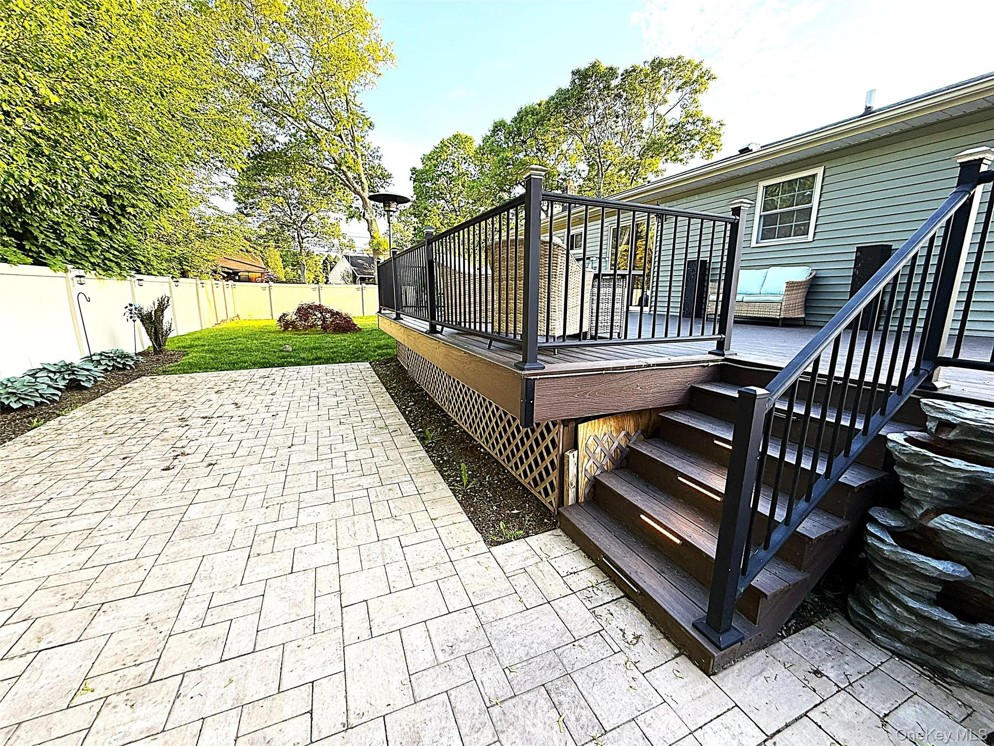 Expansive patterned patio with a wood-finish deck featuring dark railings Expansive patterned patio with a wood-finish deck featuring dark railings