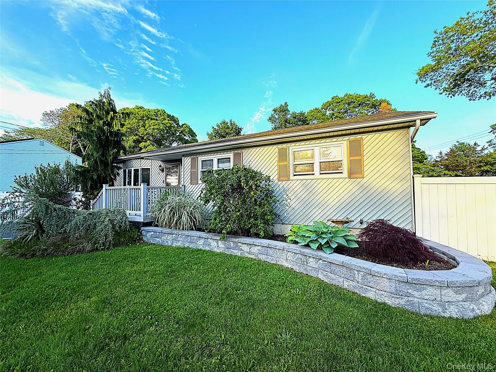 Ranch-style residence featuring horizontal siding, a front deck with railings, and a prominent stone retaining wall Ranch-style residence featuring horizontal siding, a front deck with railings, and a prominent stone retaining wall