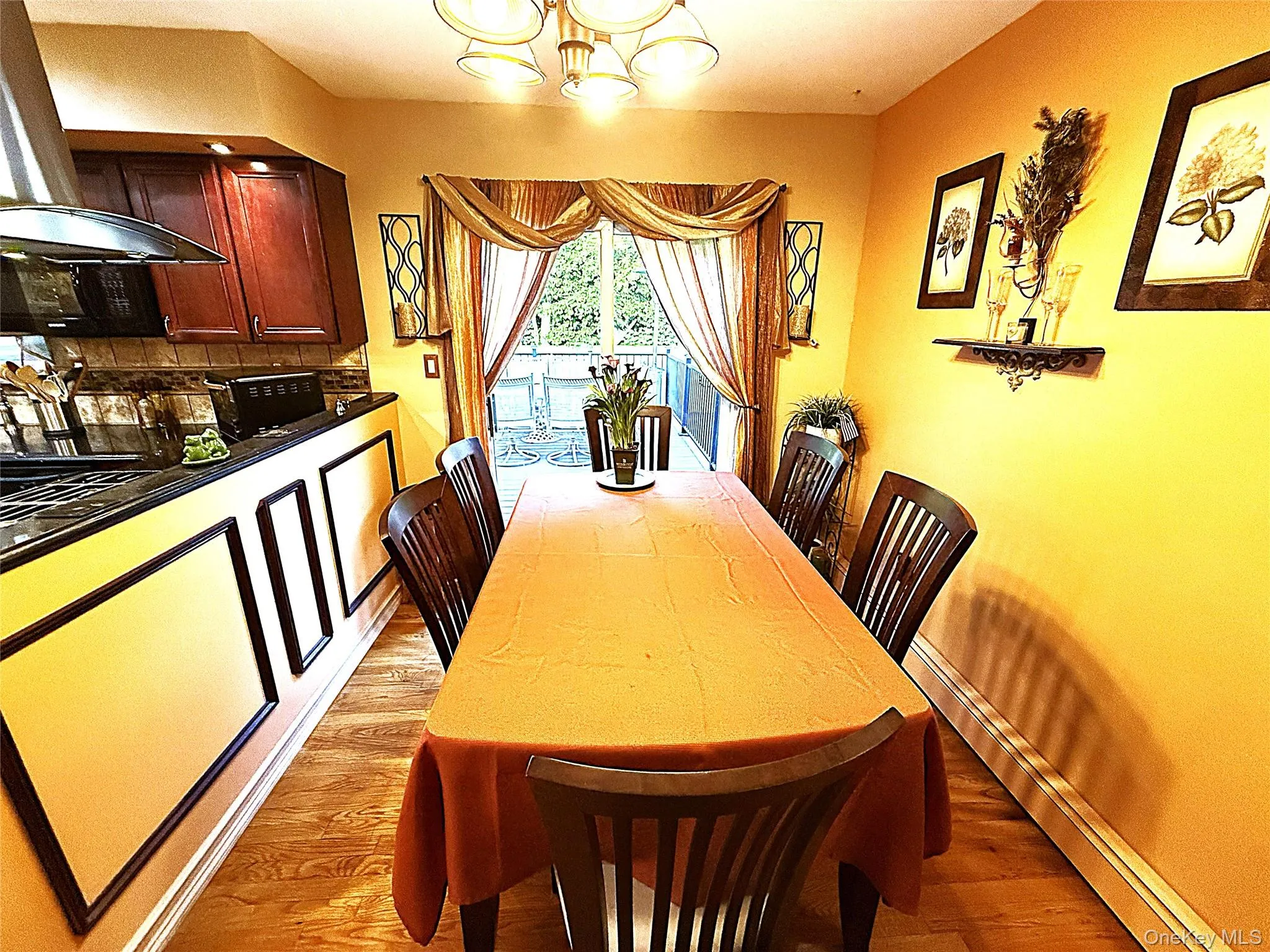Dining area with wood-finish flooring, featuring a kitchen pass-through with dark cabinetry and a dark countertop Dining area with wood-finish flooring, featuring a kitchen pass-through with dark cabinetry and a dark countertop