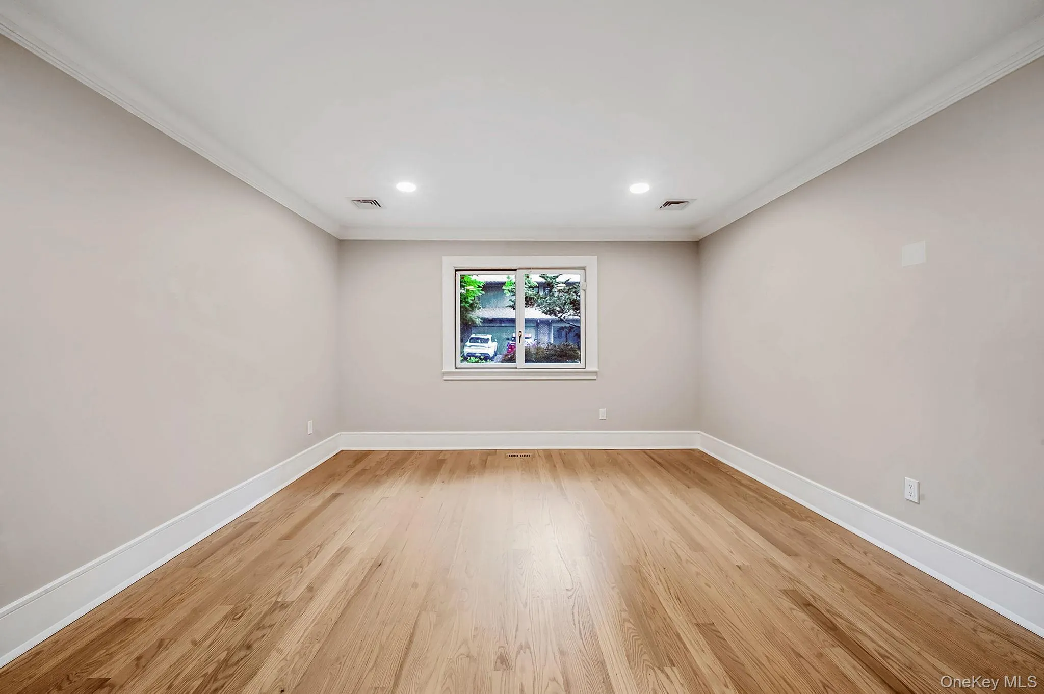 Spacious room featuring wood-finish flooring, light neutral wall tones, white trim, recessed lighting, and a window with white casing Spacious room featuring wood-finish flooring, light neutral wall tones, white trim, recessed lighting, and a window with white casing