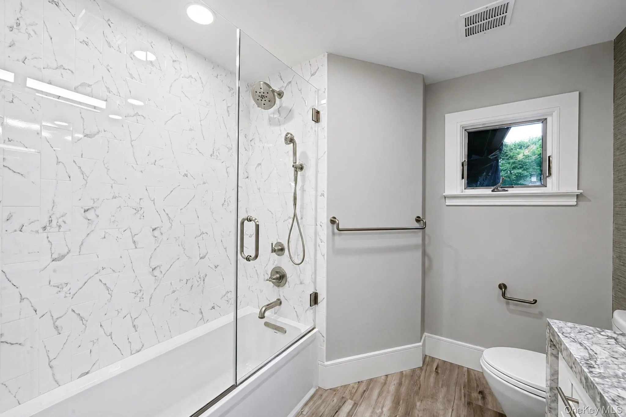 Bathtub and shower combination featuring a clear glass enclosure and large-format white marble-patterned tile surround Bathtub and shower combination featuring a clear glass enclosure and large-format white marble-patterned tile surround