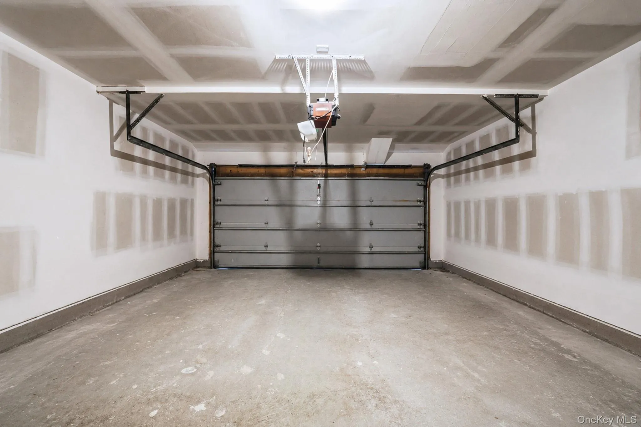 Spacious garage featuring a concrete floor, overhead lighting, and a metal sectional garage door with an automatic opener Spacious garage featuring a concrete floor, overhead lighting, and a metal sectional garage door with an automatic opener