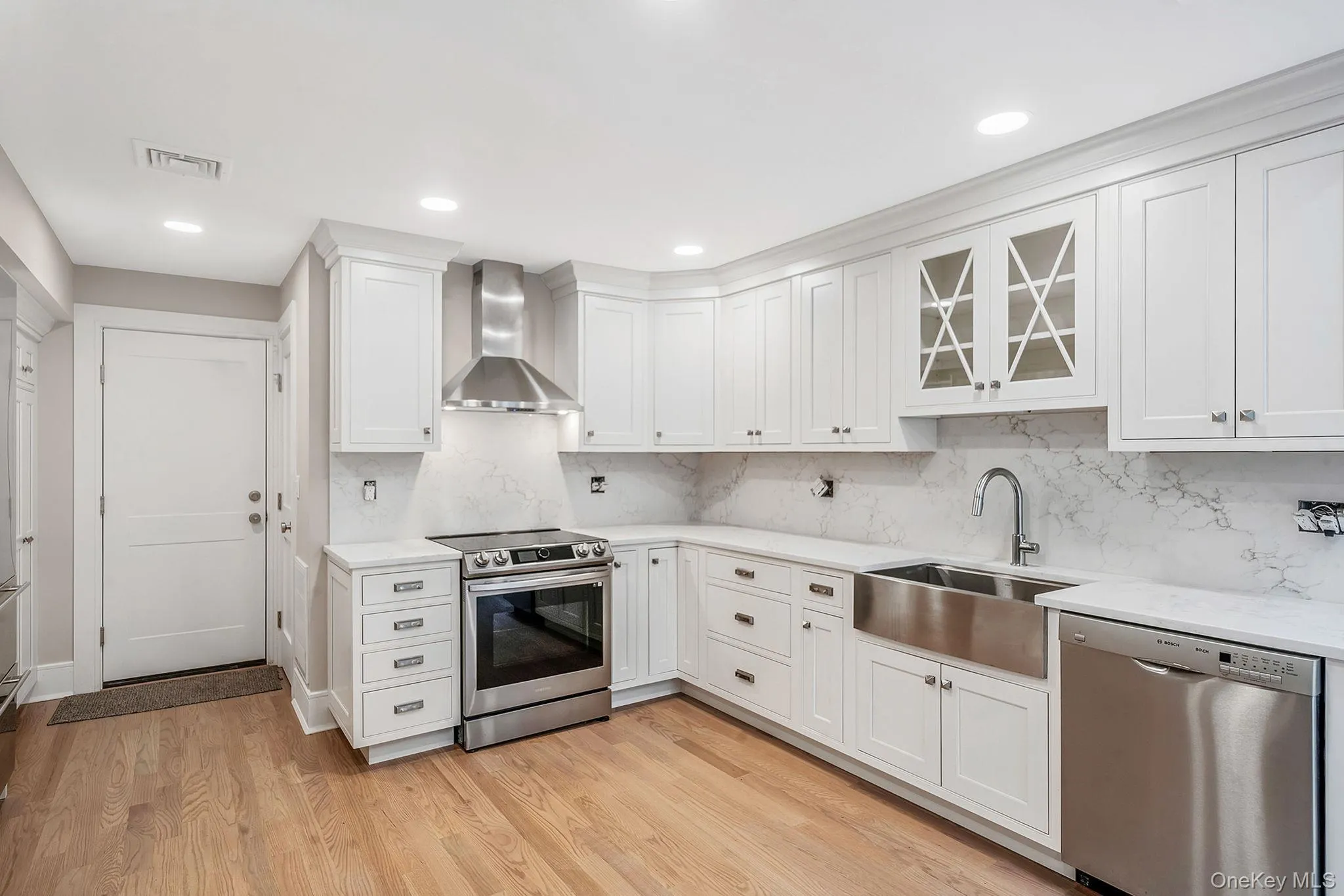 Contemporary kitchen featuring white cabinetry, light wood-finish flooring, stainless steel appliances, a stainless steel farmhouse sink, and marble-look countertops and backsplash Contemporary kitchen featuring white cabinetry, light wood-finish flooring, stainless steel appliances, a stainless steel farmhouse sink, and marble-look countertops and backsplash