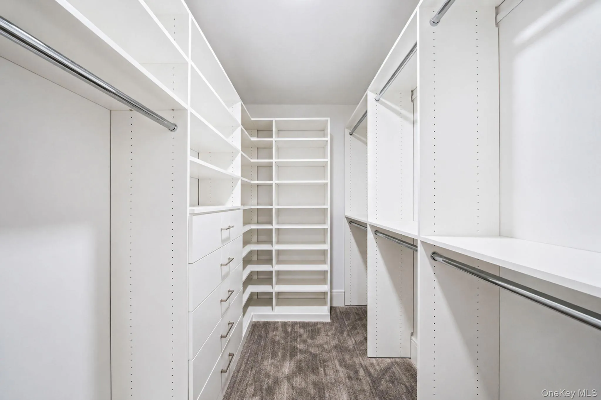 Walk-in closet featuring extensive white shelving, multiple hanging rods, built-in drawers with modern hardware, a dedicated shoe rack, and wood-finish flooring Walk-in closet featuring extensive white shelving, multiple hanging rods, built-in drawers with modern hardware, a dedicated shoe rack, and wood-finish flooring