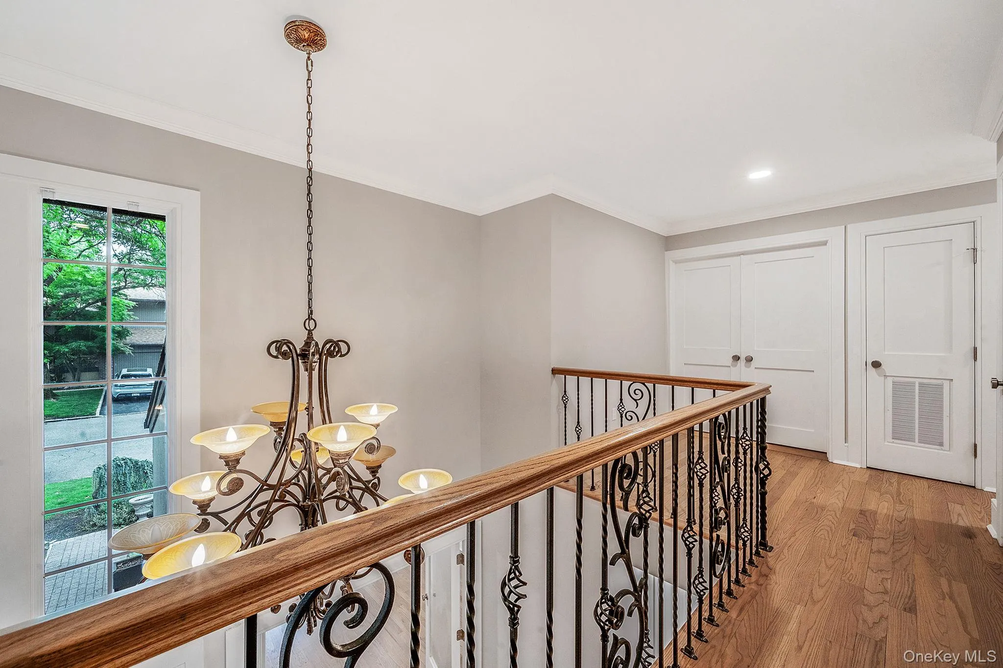 Stairwell featuring an ornate wrought iron baluster with a wood handrail, hardwood flooring, a multi-arm chandelier, and a large window Stairwell featuring an ornate wrought iron baluster with a wood handrail, hardwood flooring, a multi-arm chandelier, and a large window