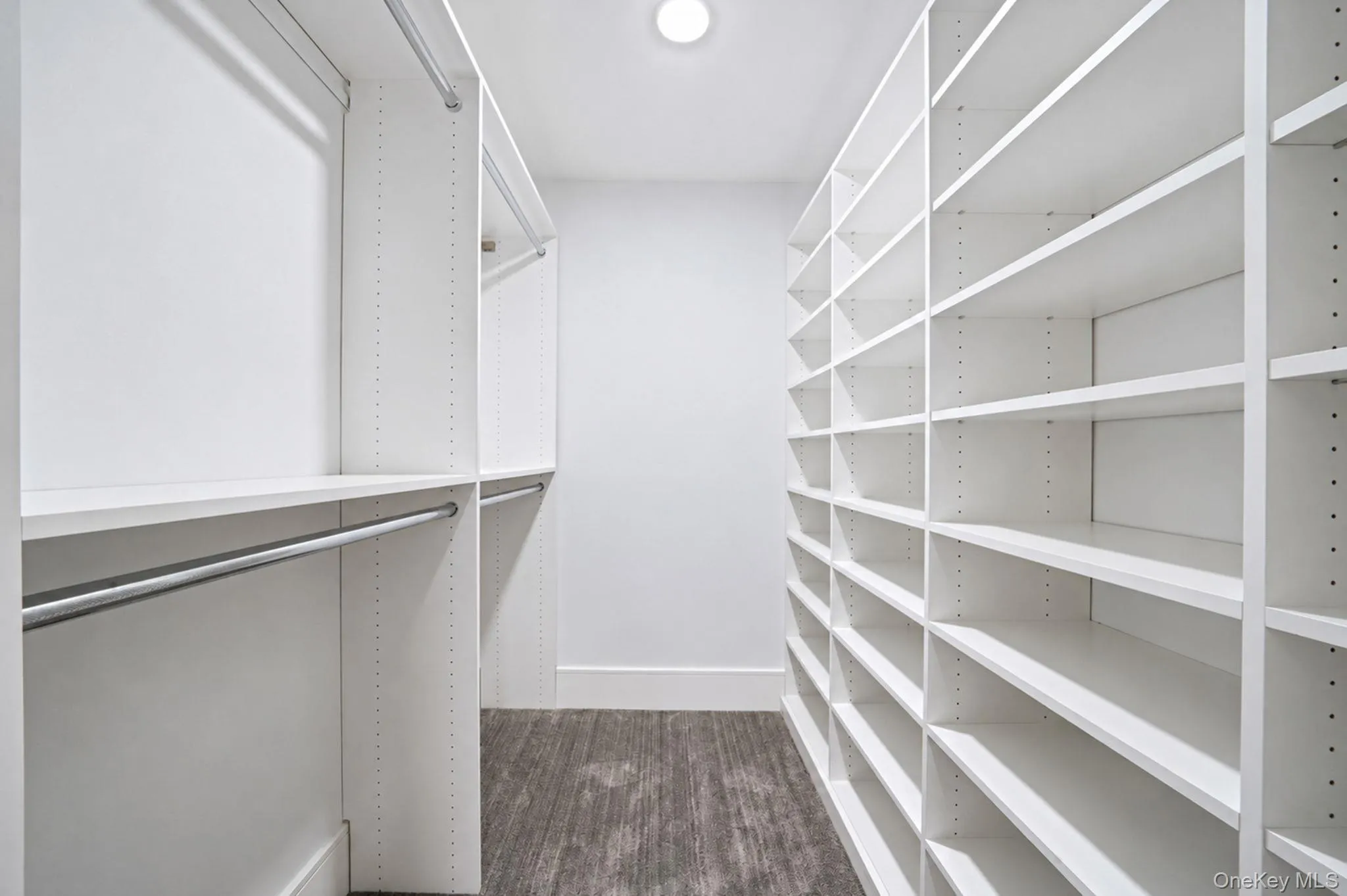 Walk-in closet featuring extensive white shelving, multiple hanging rods, and wood-finish flooring Walk-in closet featuring extensive white shelving, multiple hanging rods, and wood-finish flooring