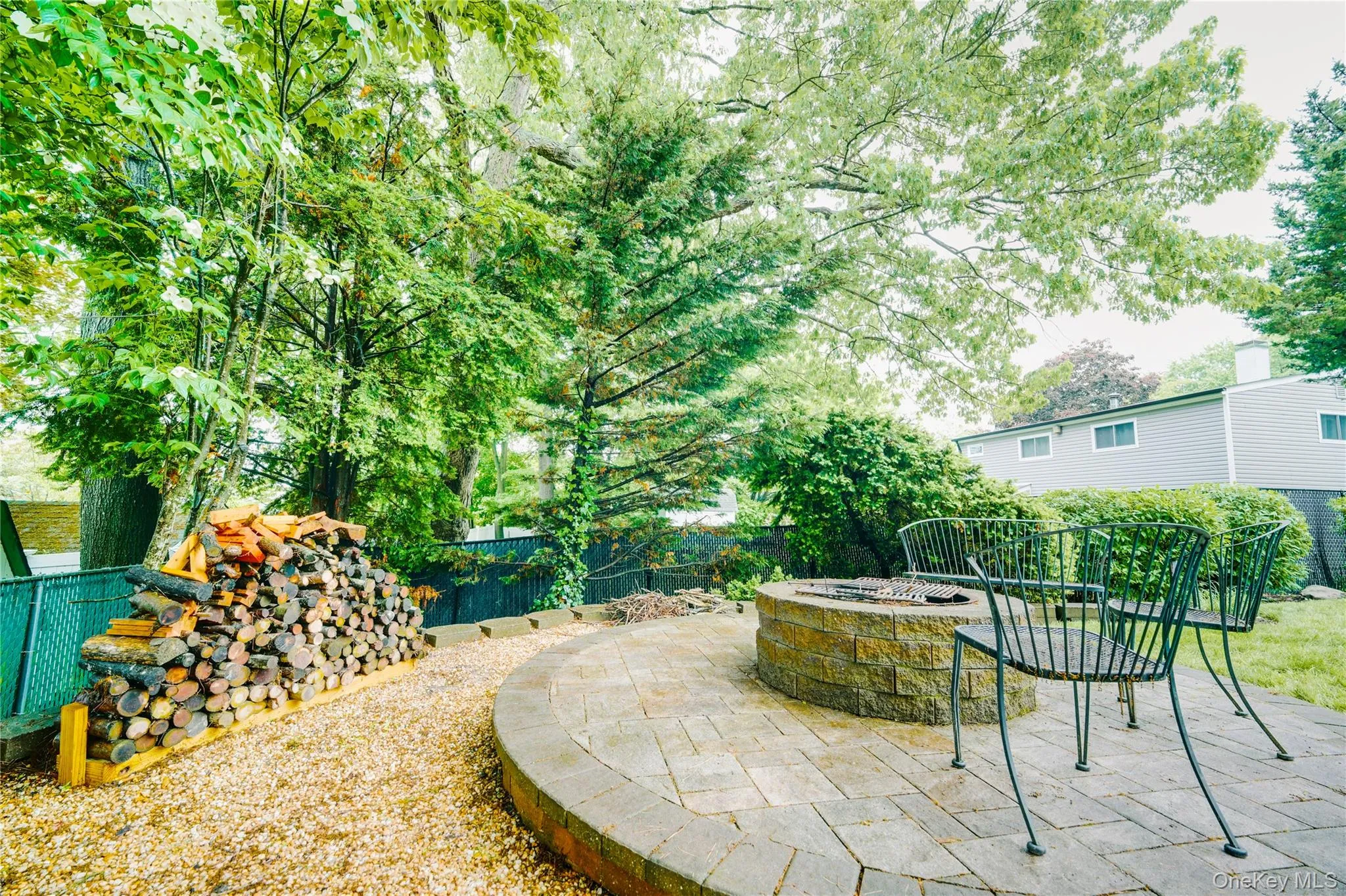 Circular paver patio with a built-in stone fire pit, surrounded by a gravel path and lush greenery Circular paver patio with a built-in stone fire pit, surrounded by a gravel path and lush greenery