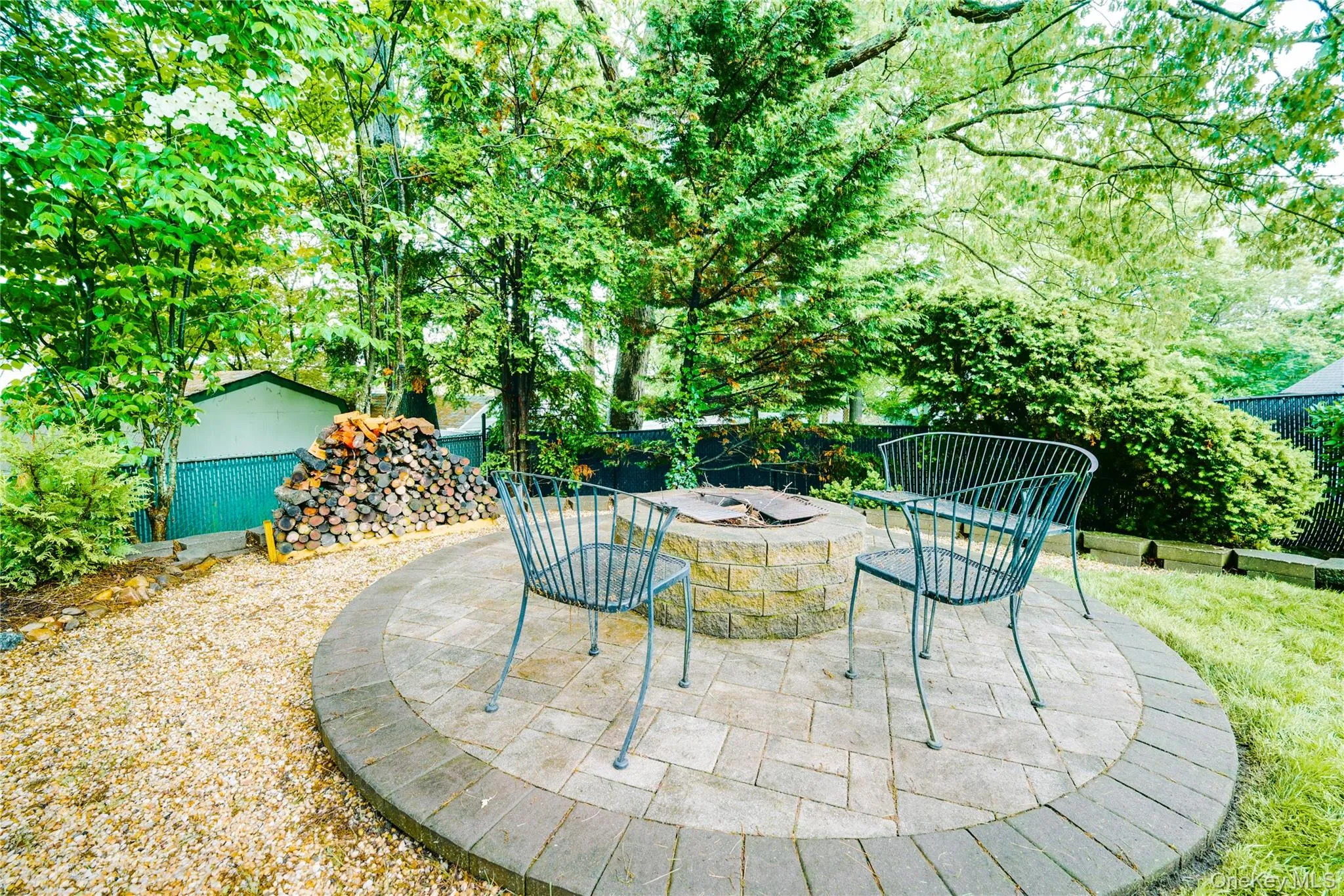 Circular paver patio with a built-in stone fire pit, surrounded by a gravel path and lush greenery Circular paver patio with a built-in stone fire pit, surrounded by a gravel path and lush greenery